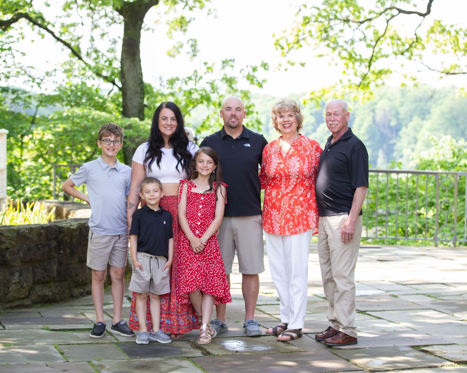 Family group poses together on stone patio wearing coordinated red and white summer outfits.