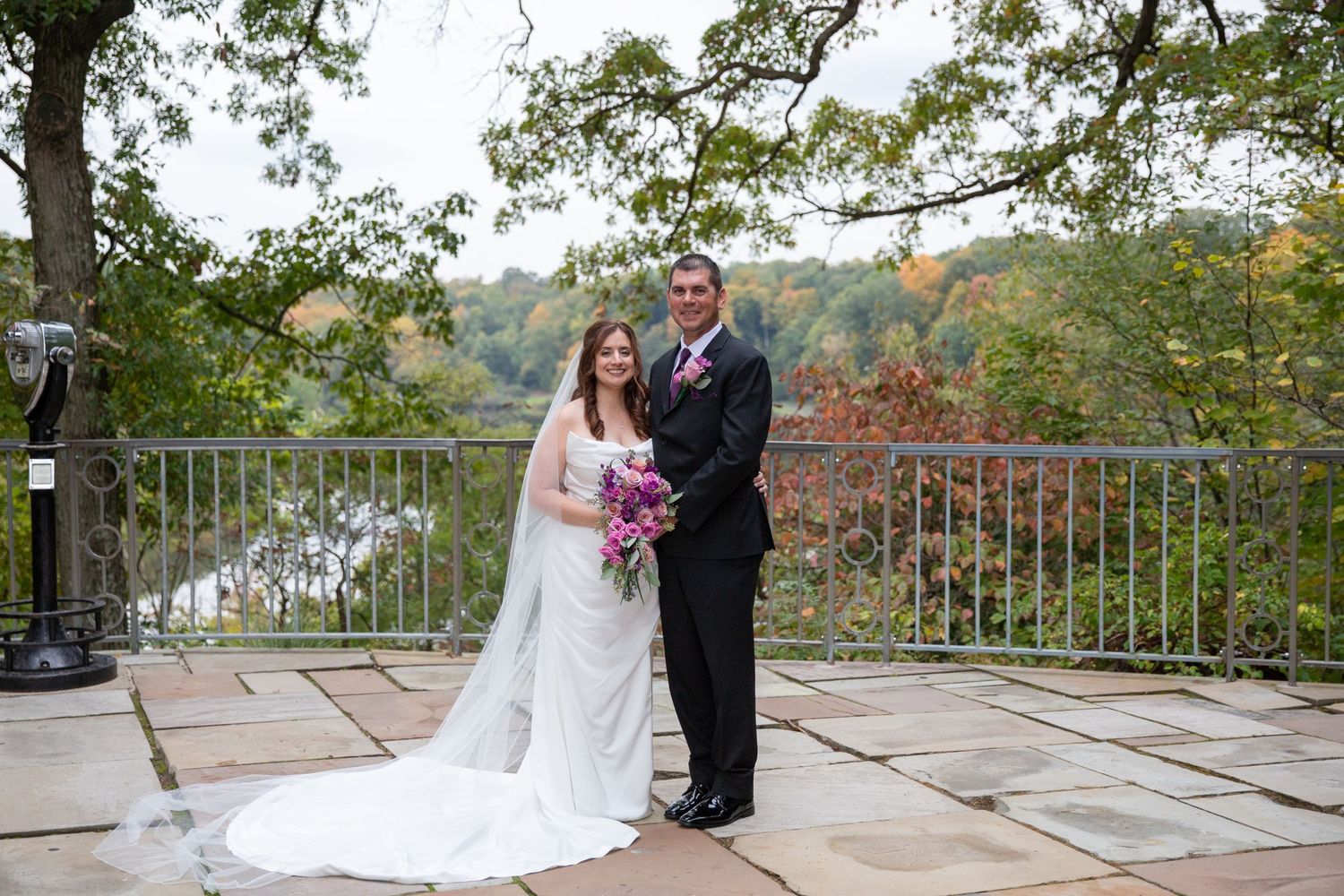 Wedding couple shares intimate moment on stone terrace overlooking autumn landscape.