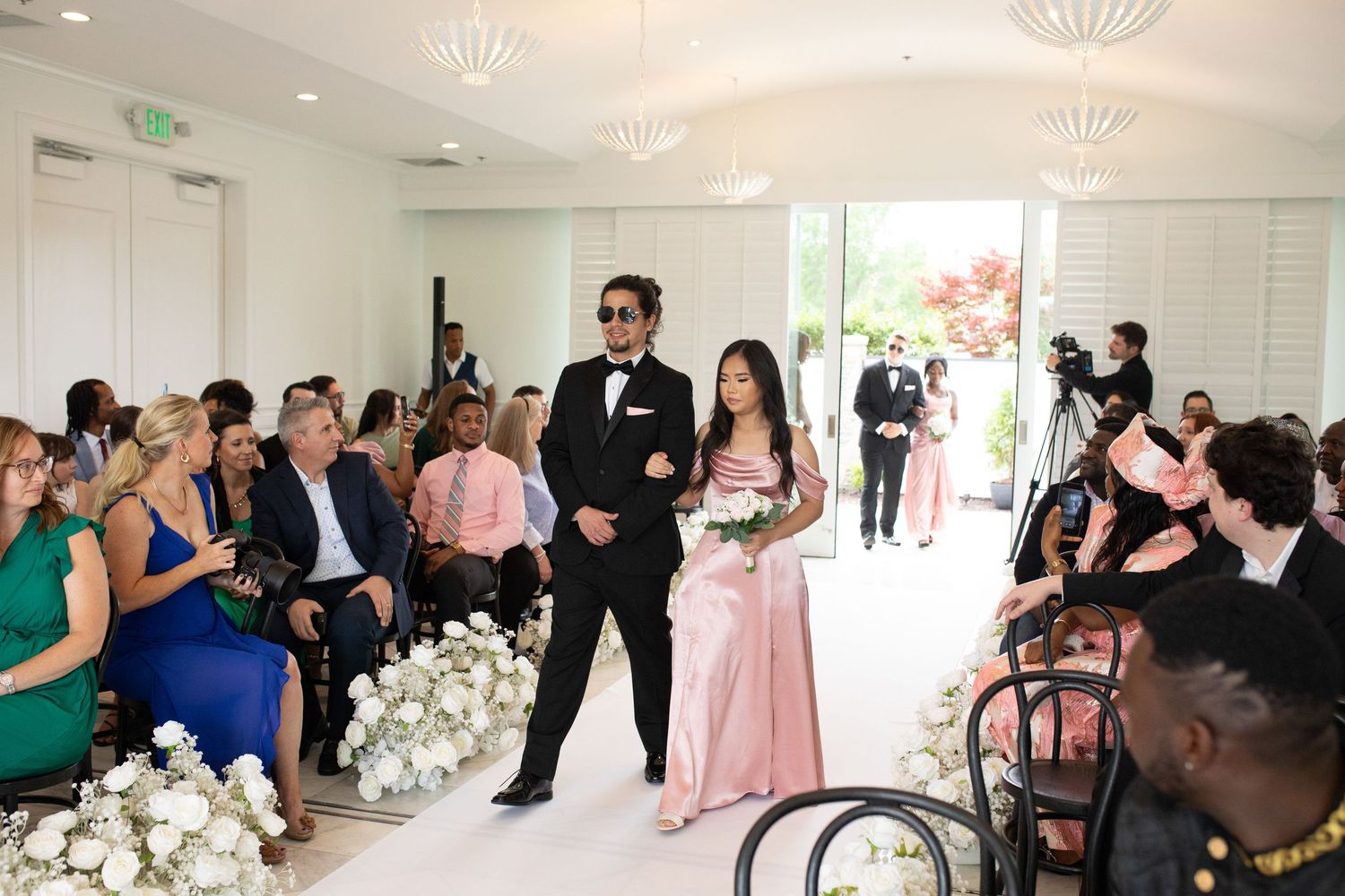 Wedding ceremony setup in a bright modern room with white floral arrangements and seated guests.