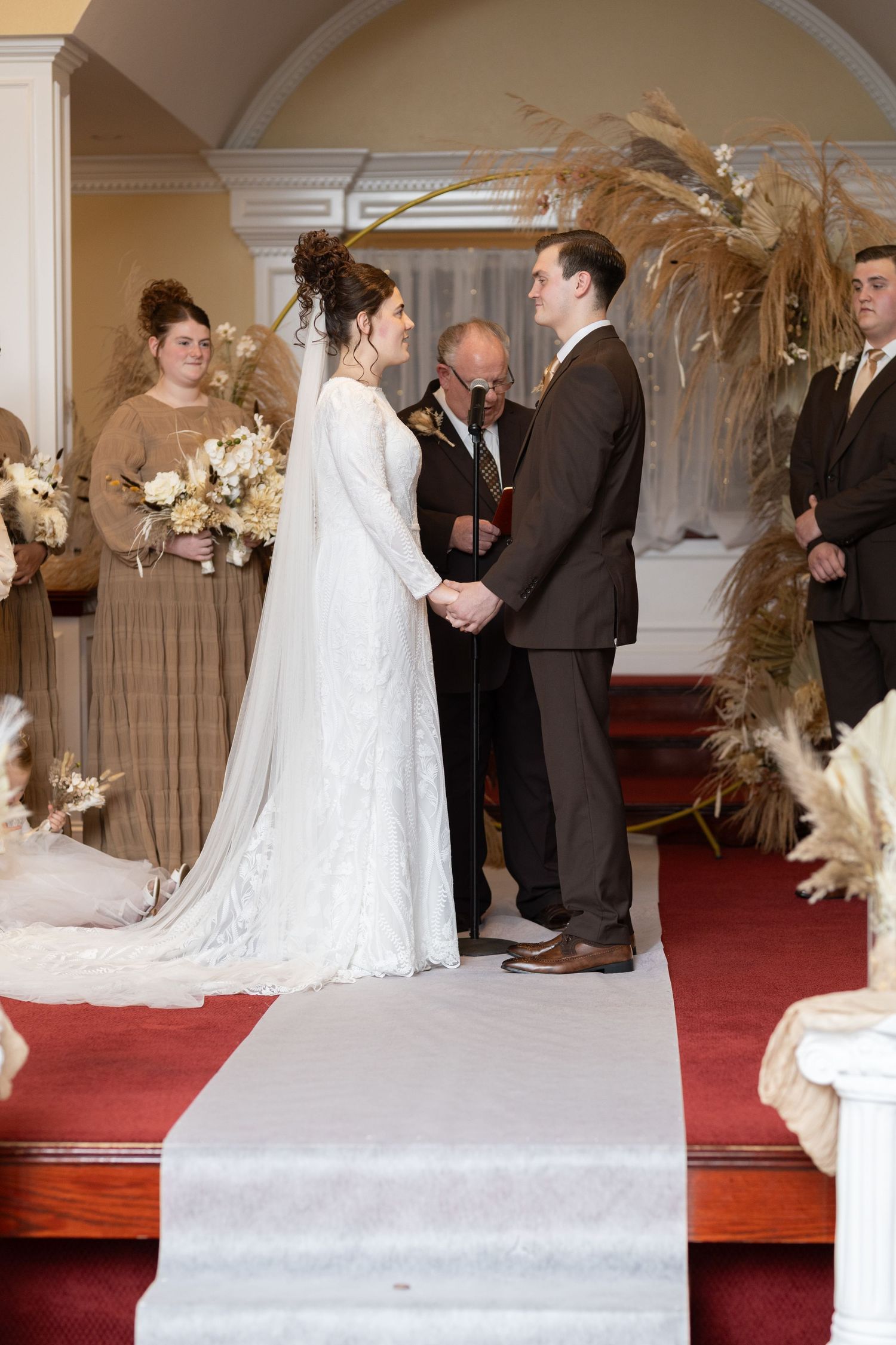 Wedding ceremony in progress with white floral decorations along a red-carpeted aisle.