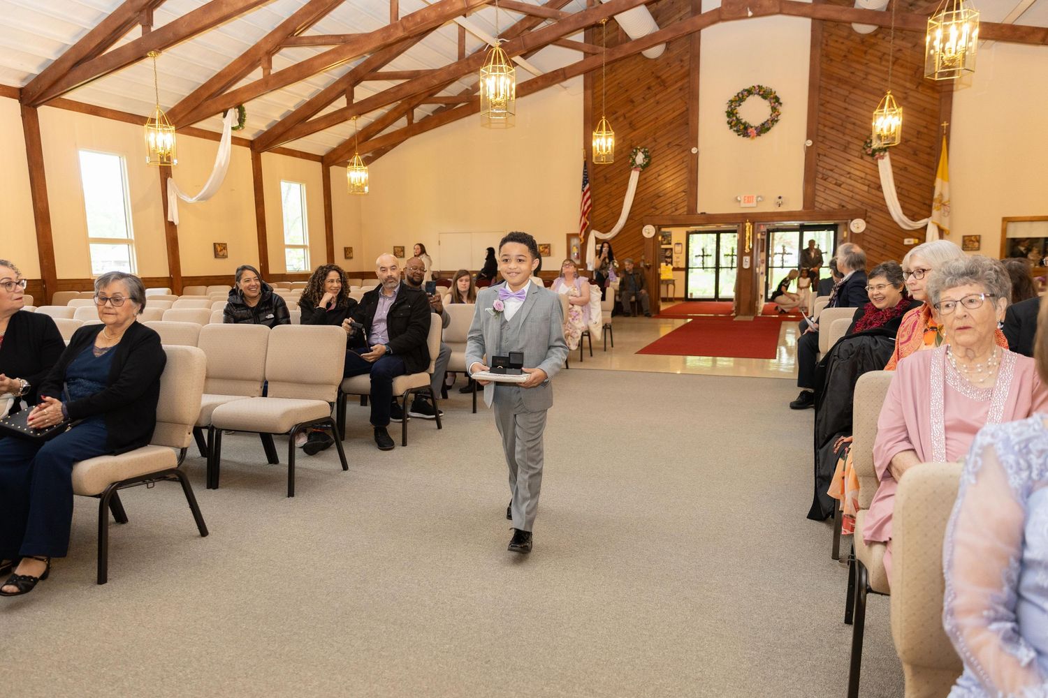 Child walking down the aisle of a decorated church hall filled with seated guests during a special ceremony.