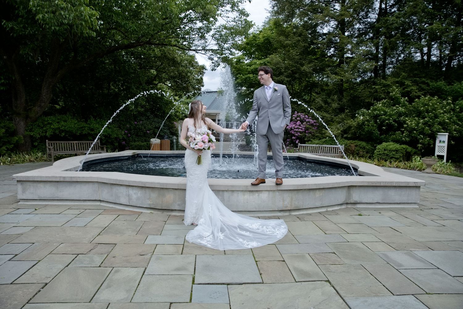 Bride and groom holding hands by an elegant garden fountain on their wedding day.