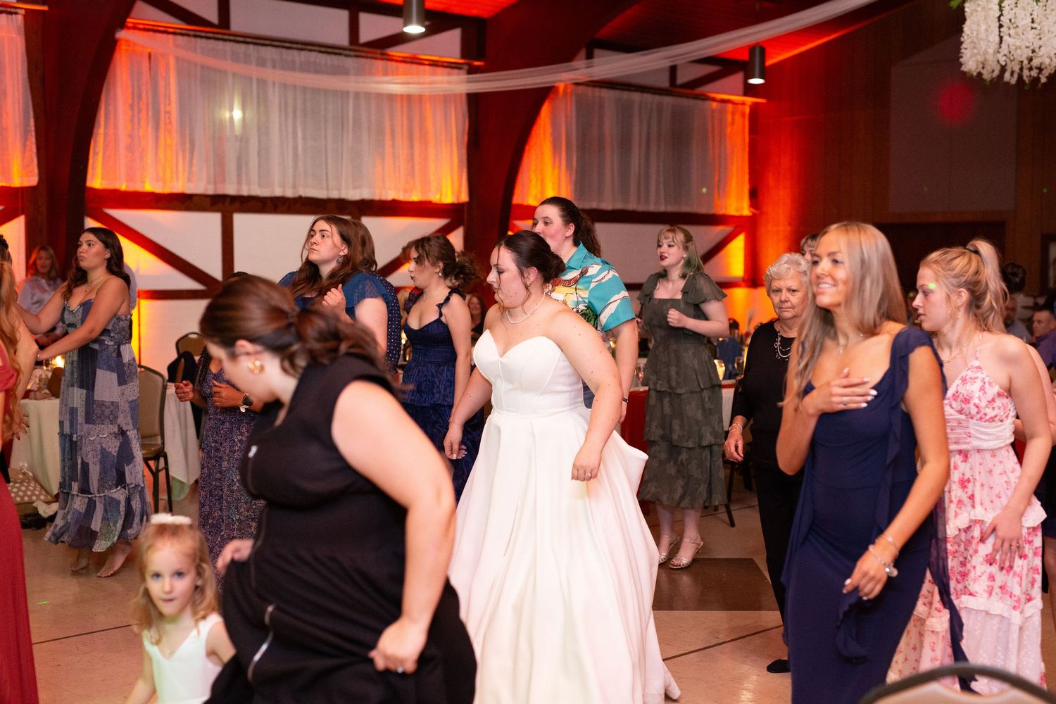 Guests dancing and celebrating at a wedding reception with orange ambient lighting.