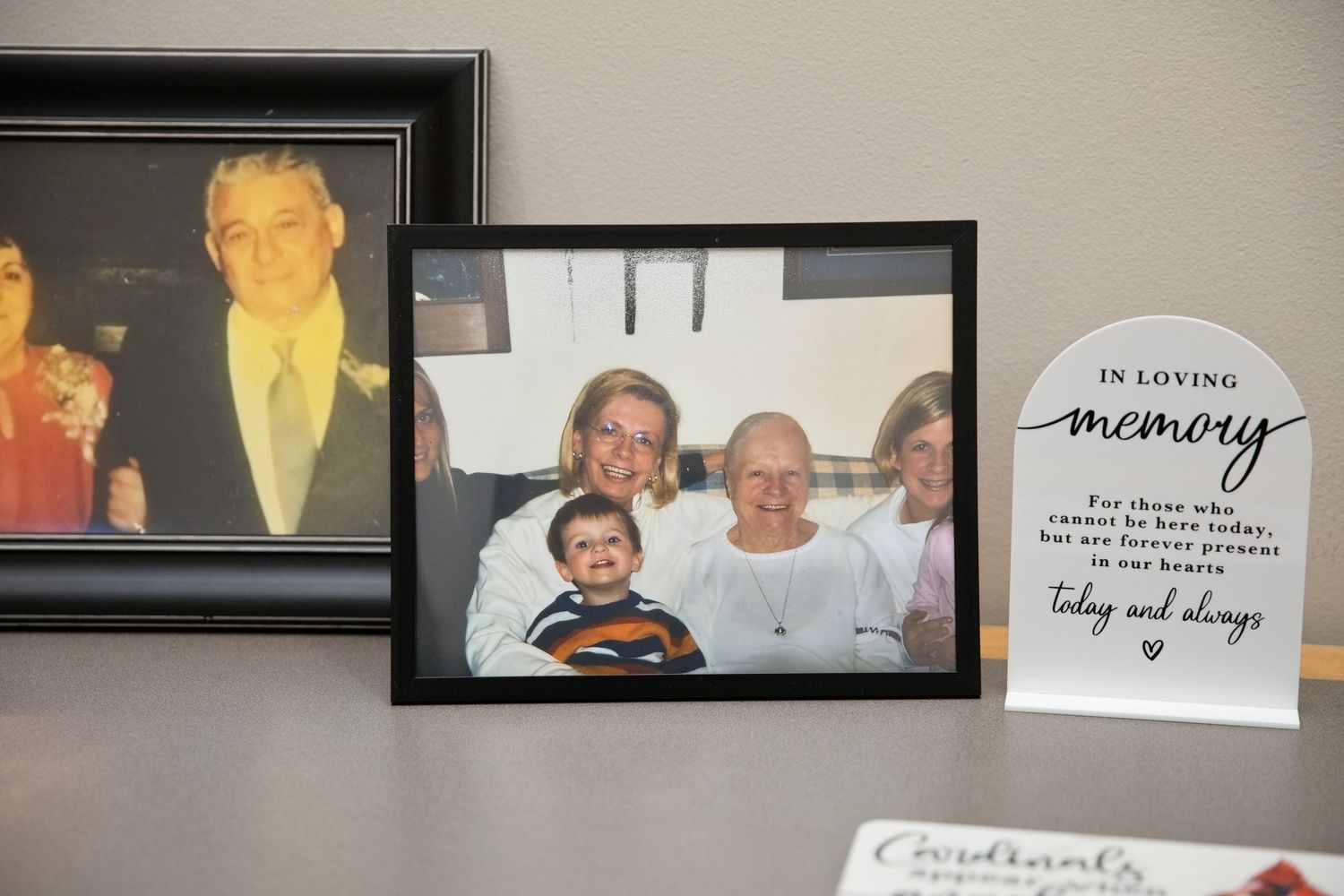 Family photos displayed on a shelf beside an In Loving Memory memorial plaque honoring a deceased loved one.