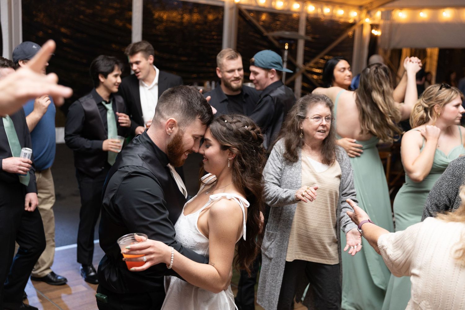 Bride and groom share a kiss on the dance floor surrounded by wedding guests at a festive indoor reception.