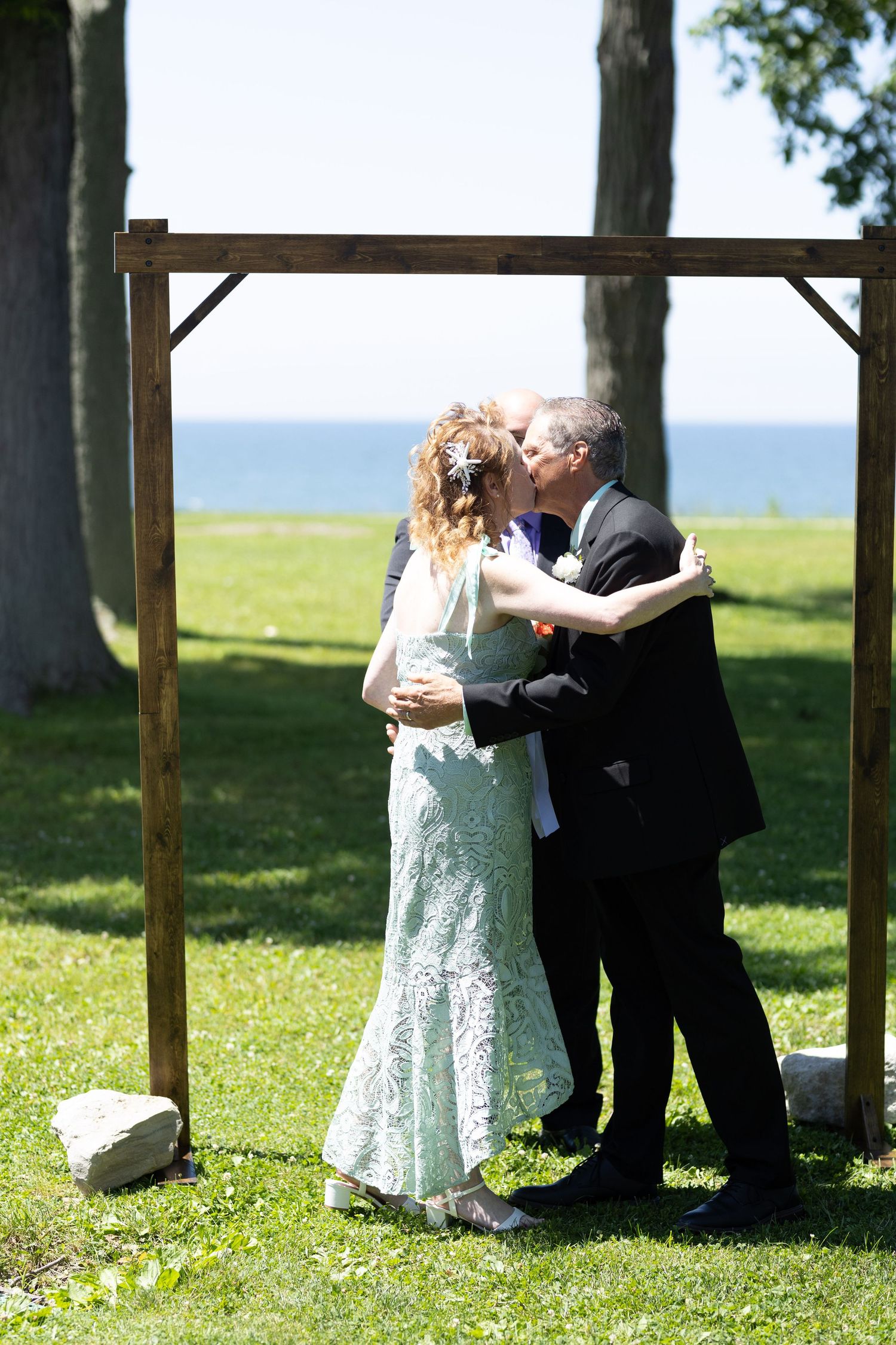 Intimate outdoor wedding ceremony with wooden arch and natural landscape backdrop.