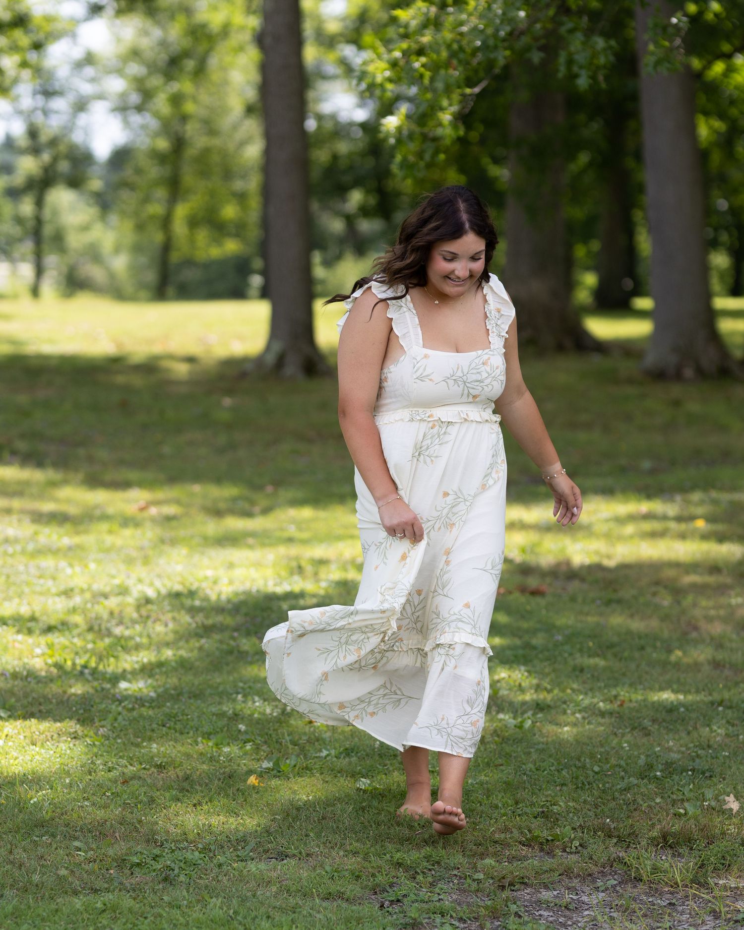 A flowing white sundress twirls gracefully in a sunlit park setting with tall trees in the background.