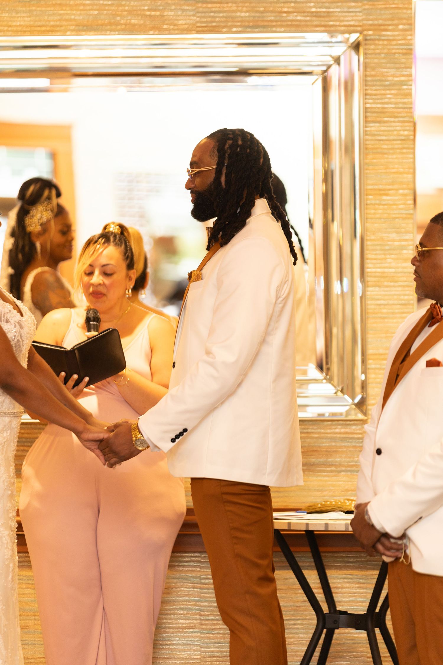 Wedding party members in pink dresses and white suits gather for formal photos.