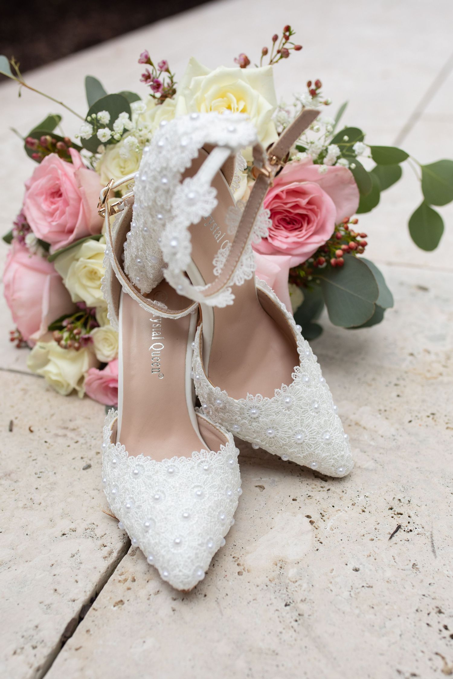 Elegant white beaded bridal shoes displayed with pink and cream roses.