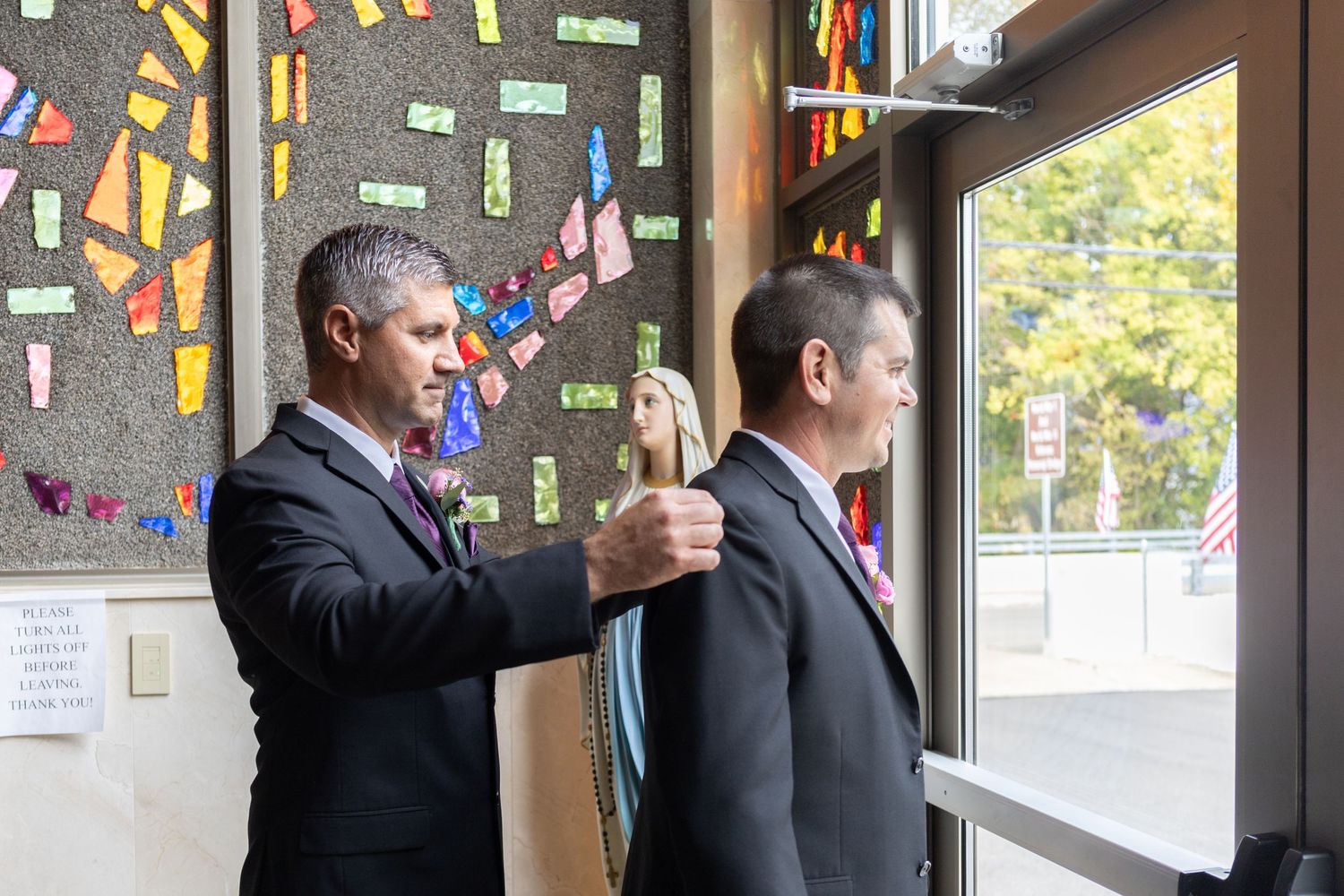 Man in formal attire standing by window with colorful decorations.