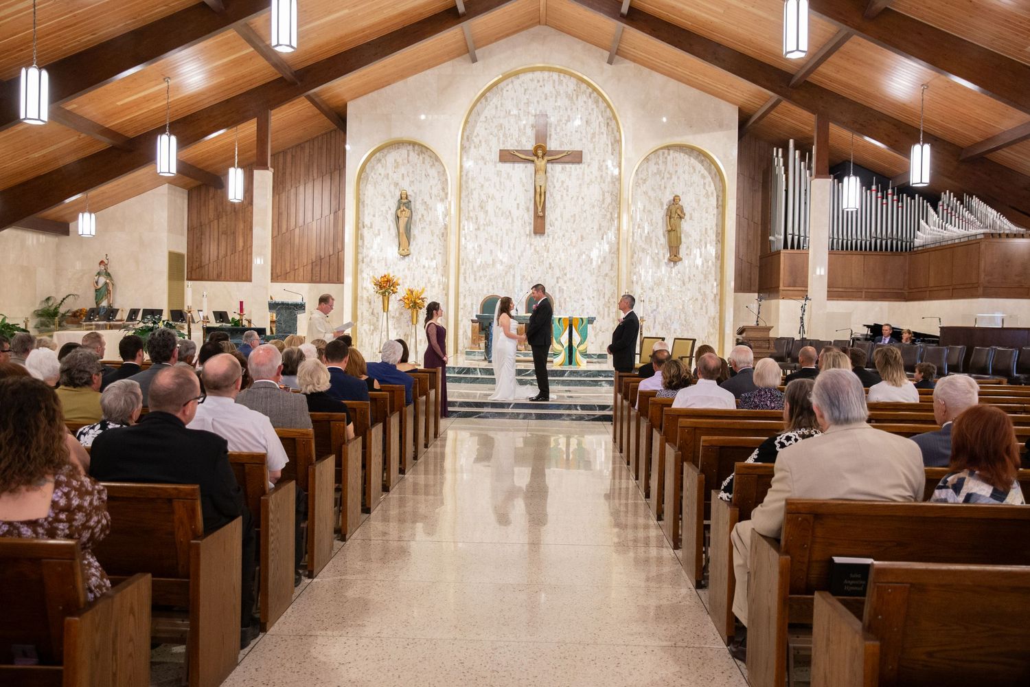 Wide view of church sanctuary with wooden pews and vaulted ceiling during ceremony.
