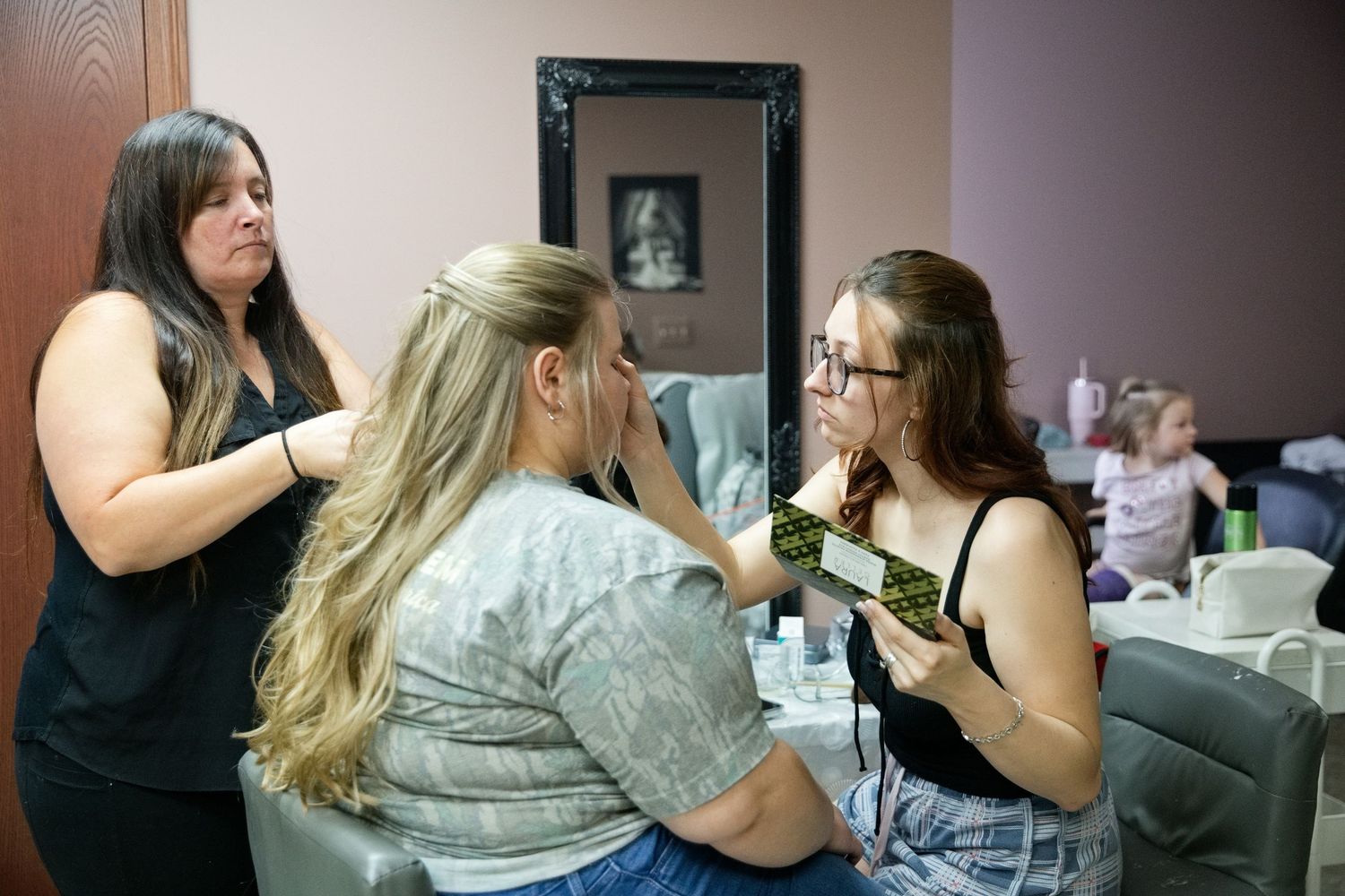 A makeup artist applies cosmetics to a client while another woman observes in a beauty salon setting.