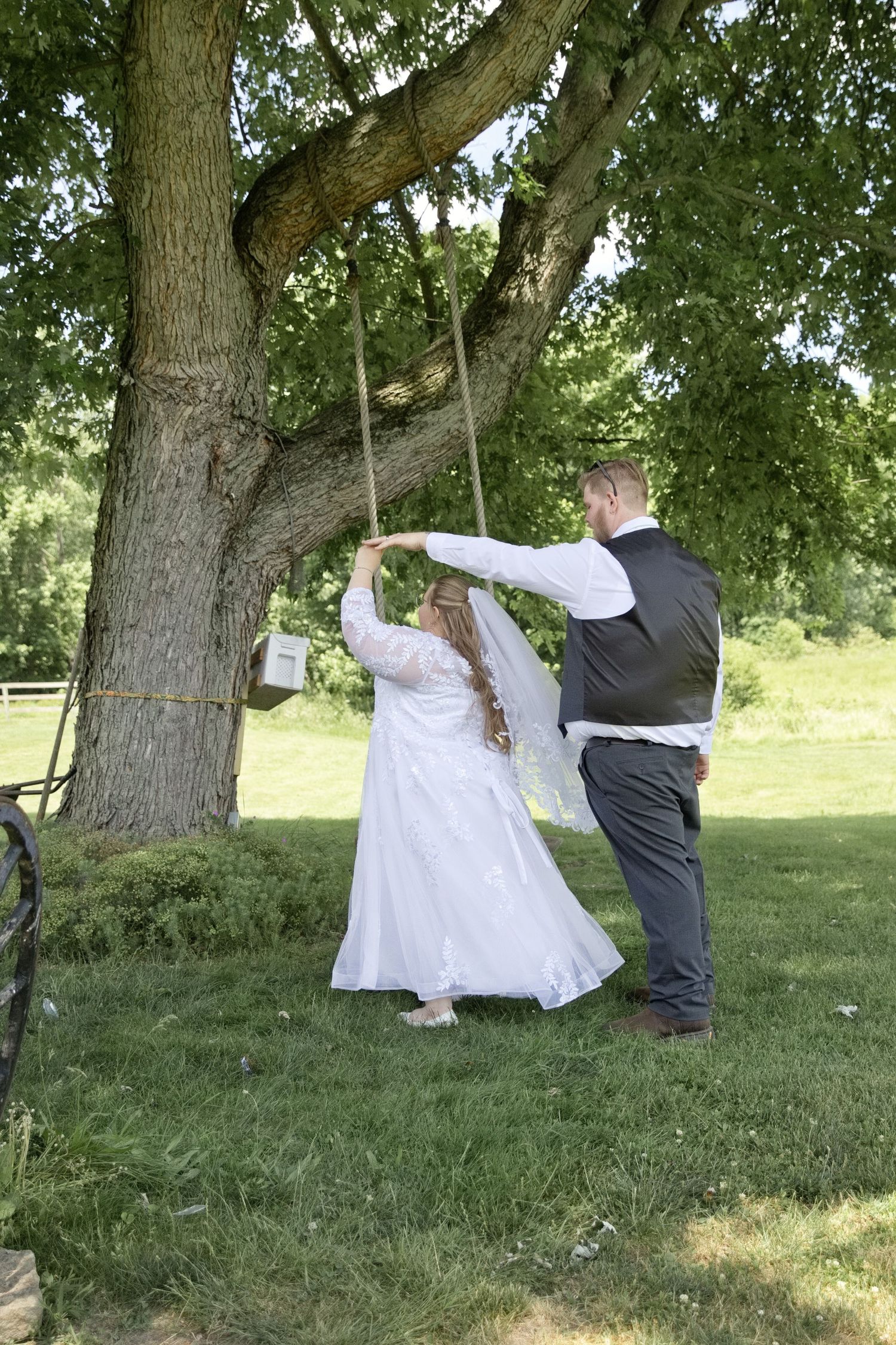 Bride and groom sharing a romantic moment on a rope swing under a large tree outdoors on their wedding day.