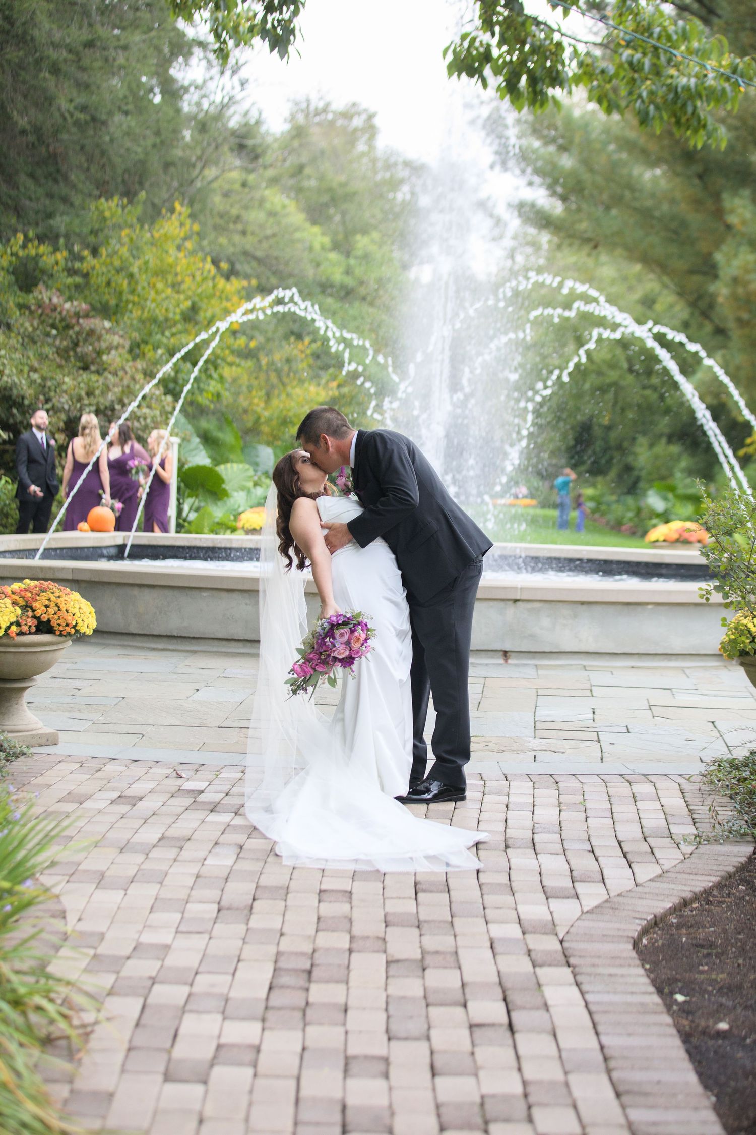 Wedding portraits by fountain with water features and brick pathway.