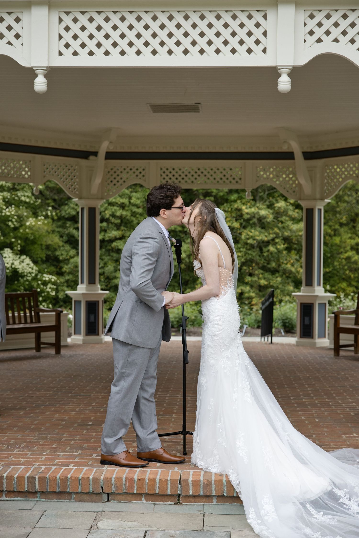 Bride and groom share their first kiss under an elegant white gazebo during their outdoor wedding ceremony.