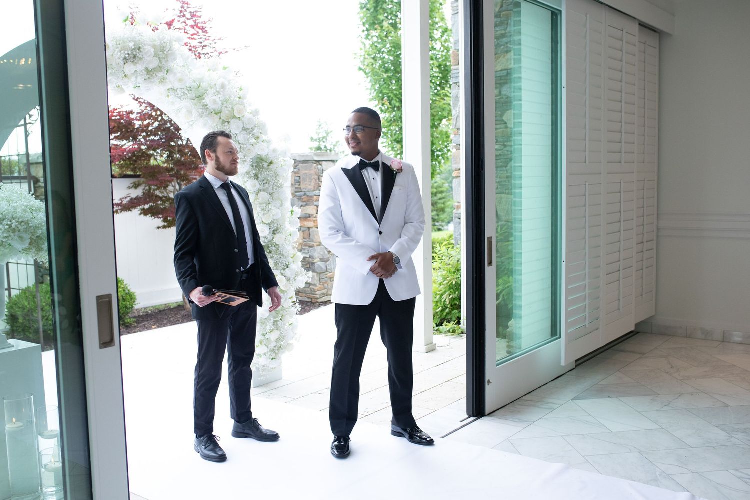 Wedding party members in formal attire stand in a modern hallway with glass windows.
