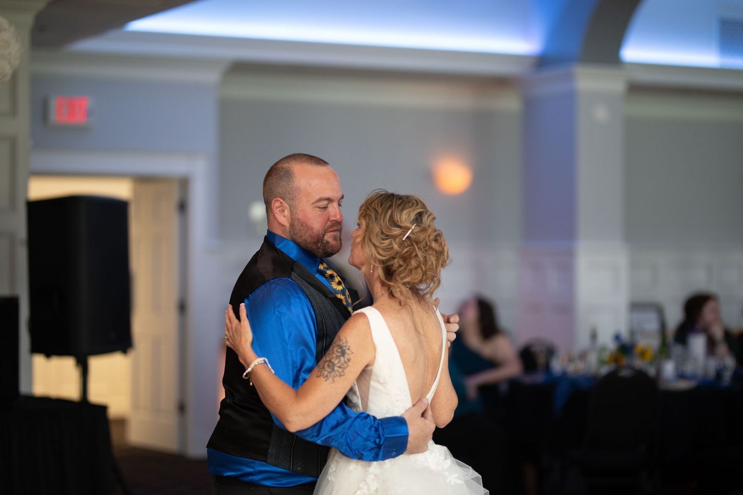 Bride and groom share their first dance at a wedding reception in an elegant ballroom with blue lighting.
