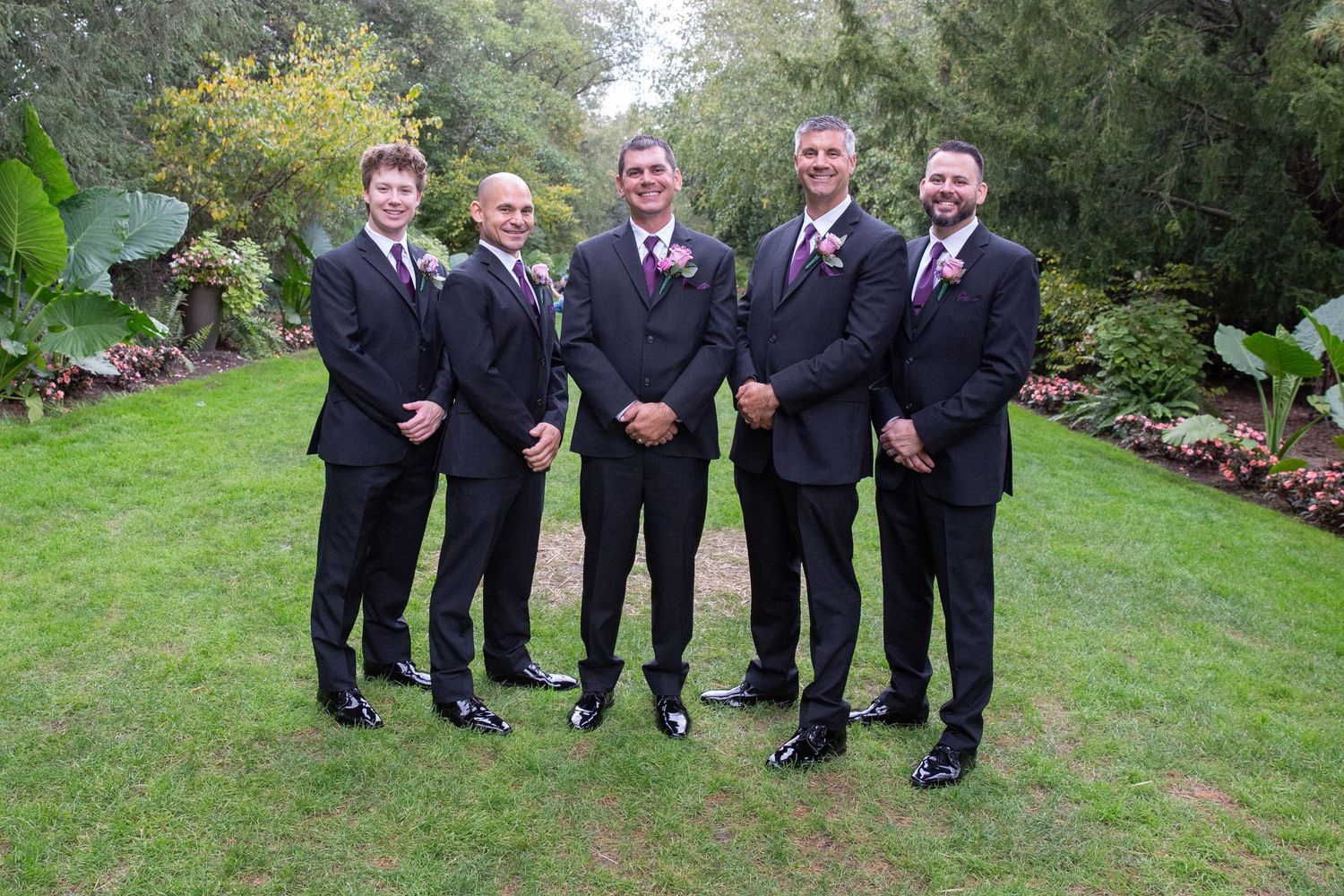 Groomsmen in black suits with pink accents posing in garden setting.