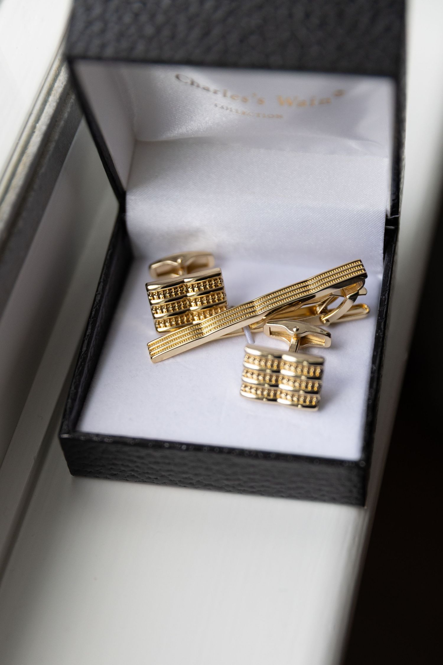 Gold tie clips and cufflinks displayed in a black jewelry box.