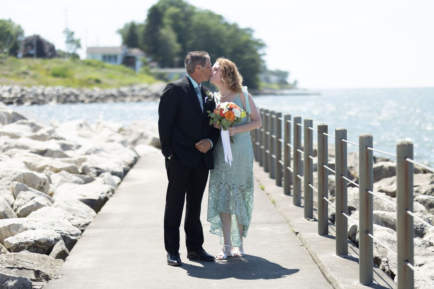 Wedding couple walking along a scenic waterfront path with wooden railings.