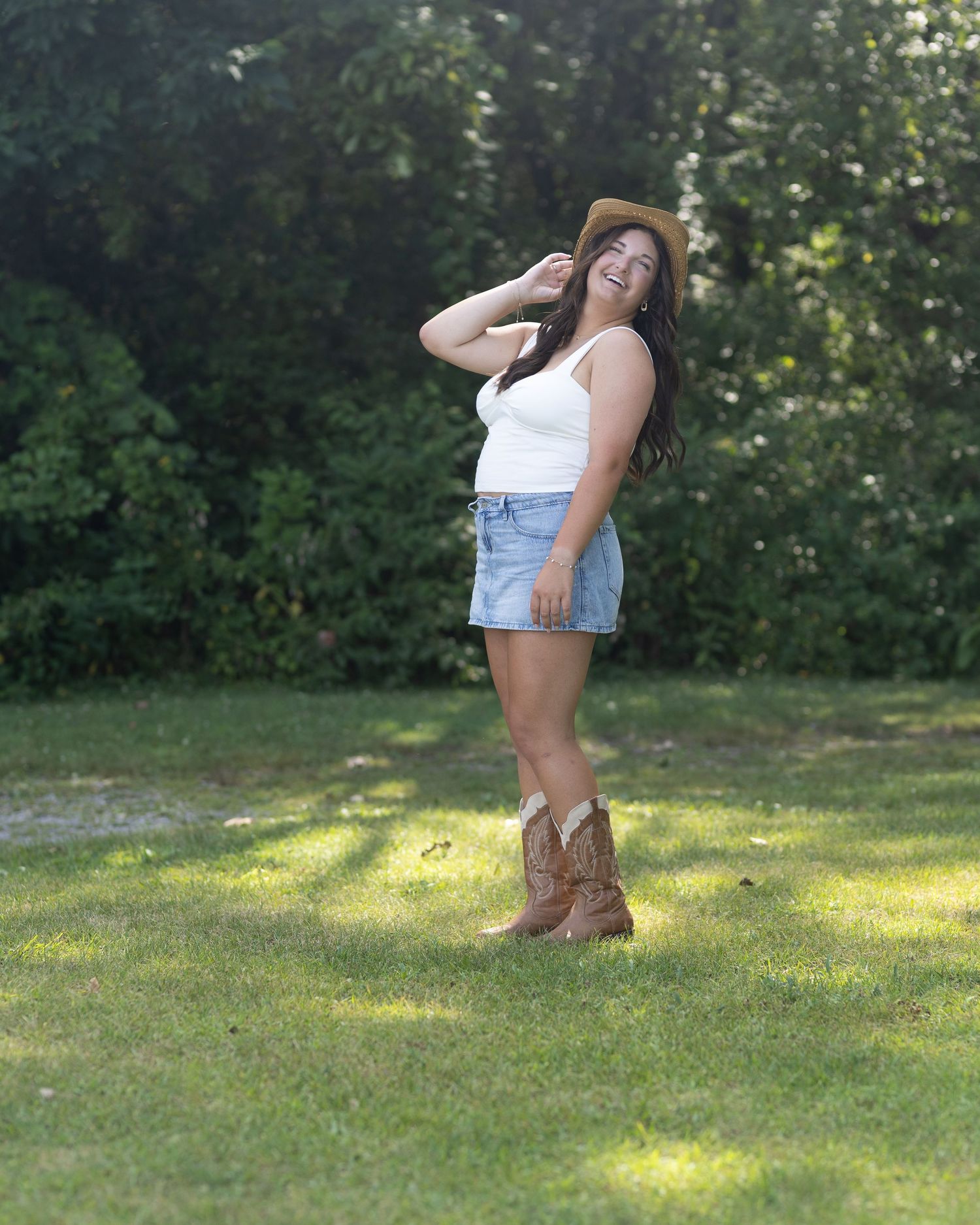 Country-inspired look with cowboy boots and straw hat in a sunlit garden setting.