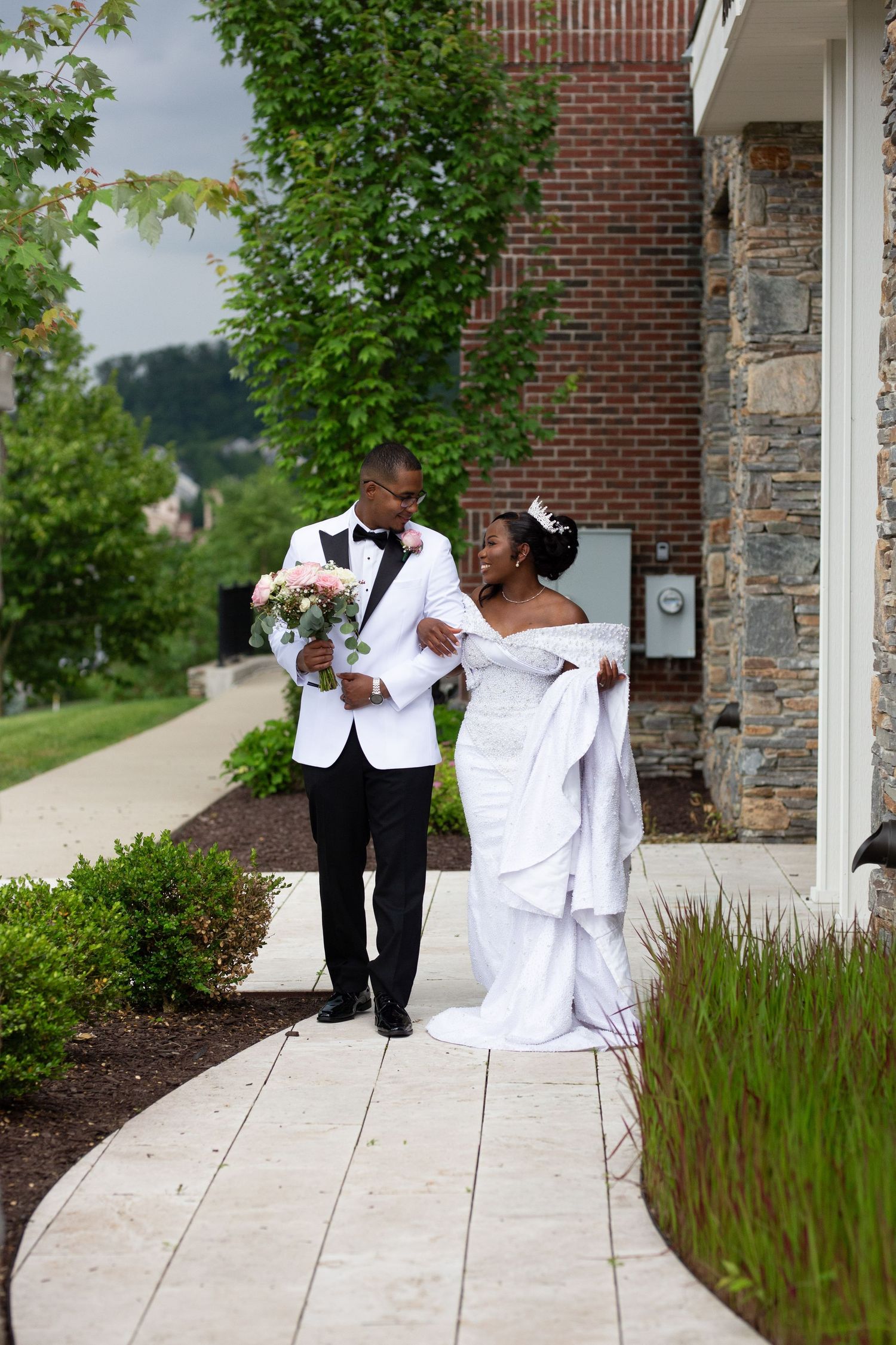 Wedding couple sharing romantic moments along stone walkway with landscaped gardens.
