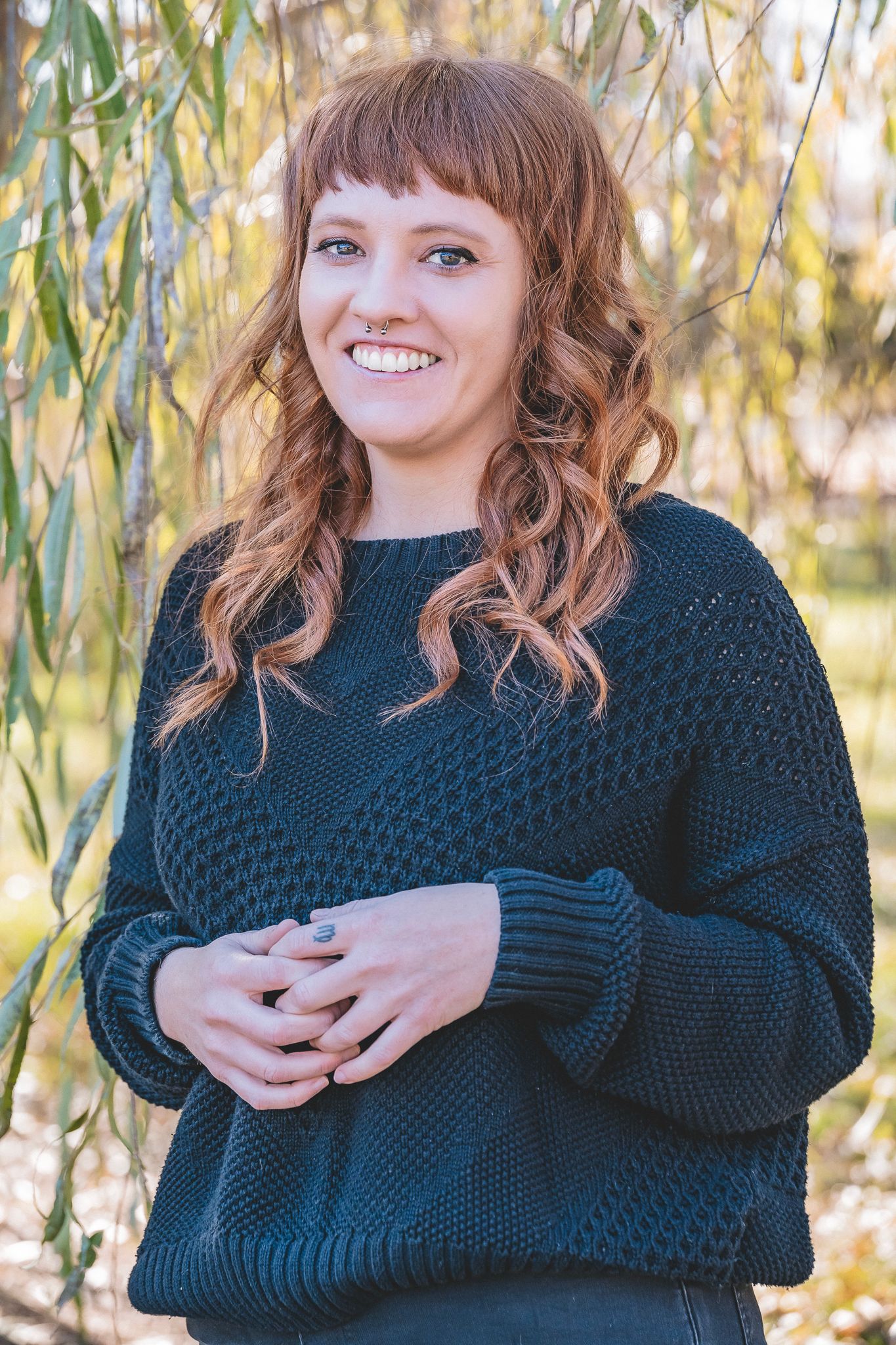Smiling young woman with curly red hair wearing a dark knit sweater outdoors in autumn.