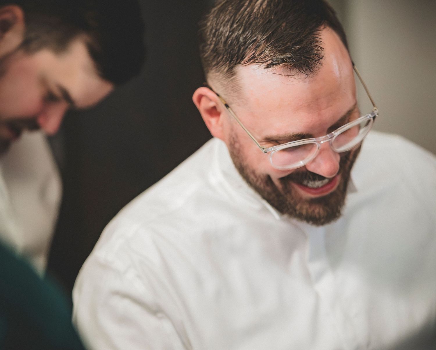 Smiling bearded man in white shirt with clear glasses in candid indoor portrait.