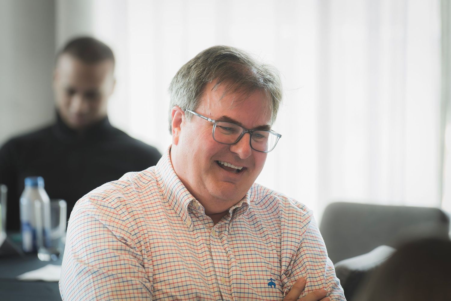 Laughing businessman with glasses in checkered shirt at corporate meeting or workshop.