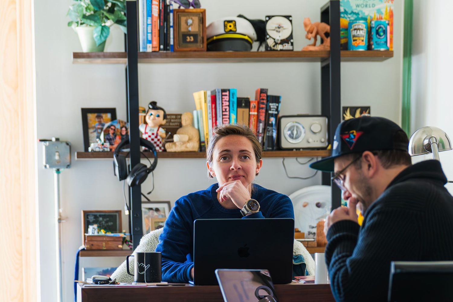 Team meeting with three people discussing around laptops near a whiteboard in an office.
