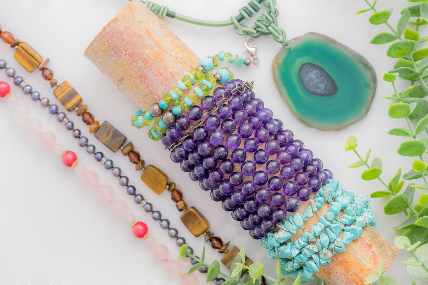 Flat lay of purple amethyst bracelet, turquoise chips, and mixed gemstone jewelry pieces.
