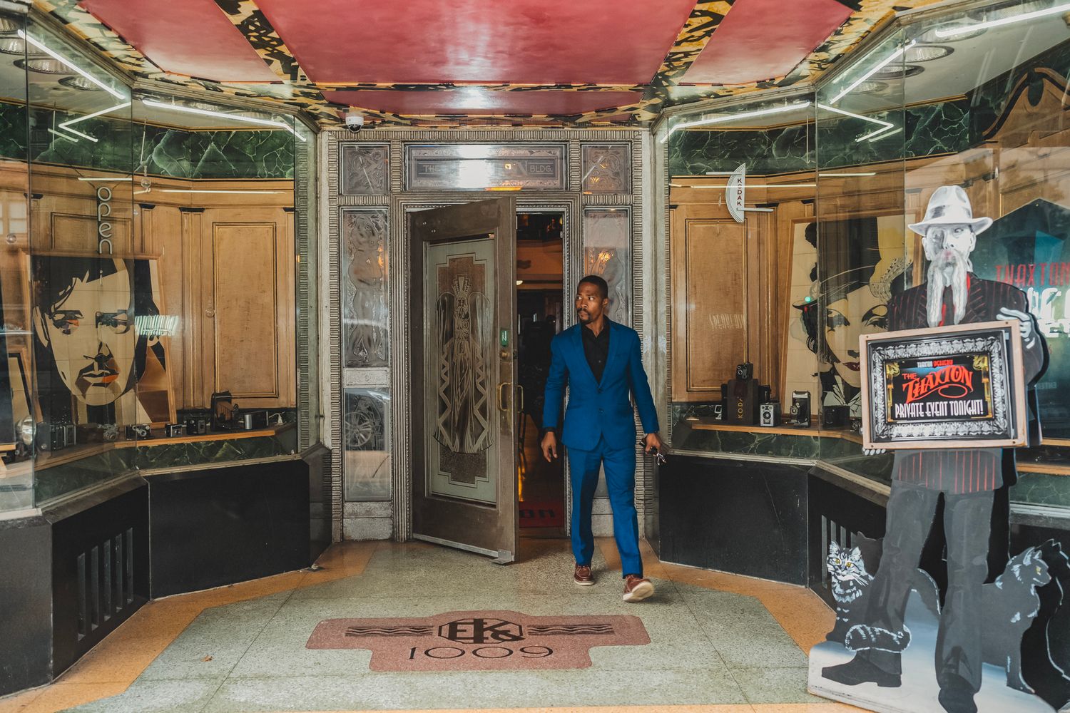 Stylish man in blue suit exiting ornate vintage elevator in decorated lobby.