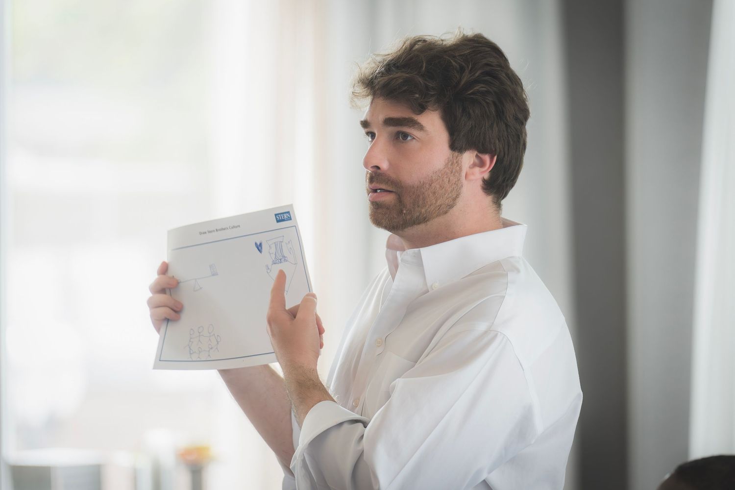 Young bearded man in white shirt holds document during professional business presentation.