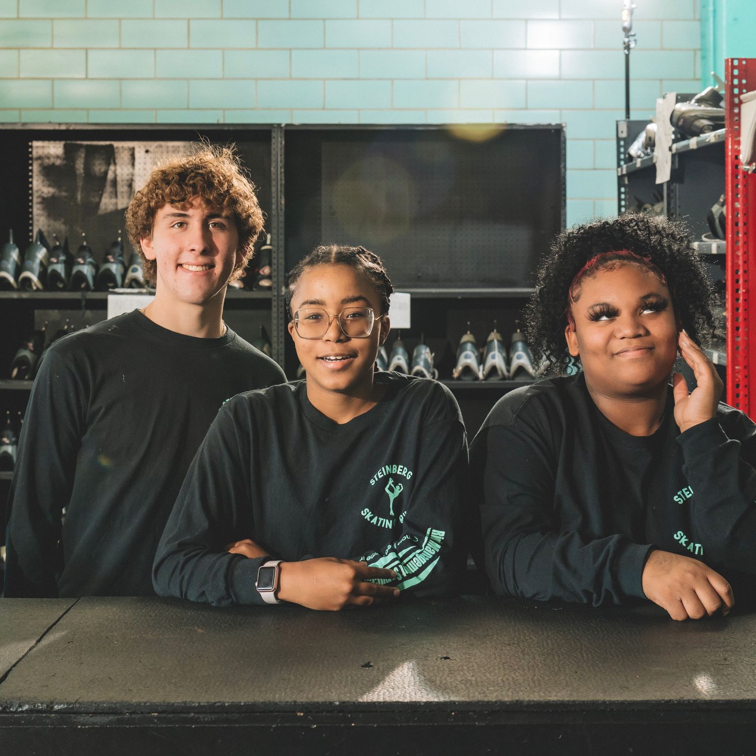 Three young people in matching dark green shirts smile together behind a counter in a modern venue.