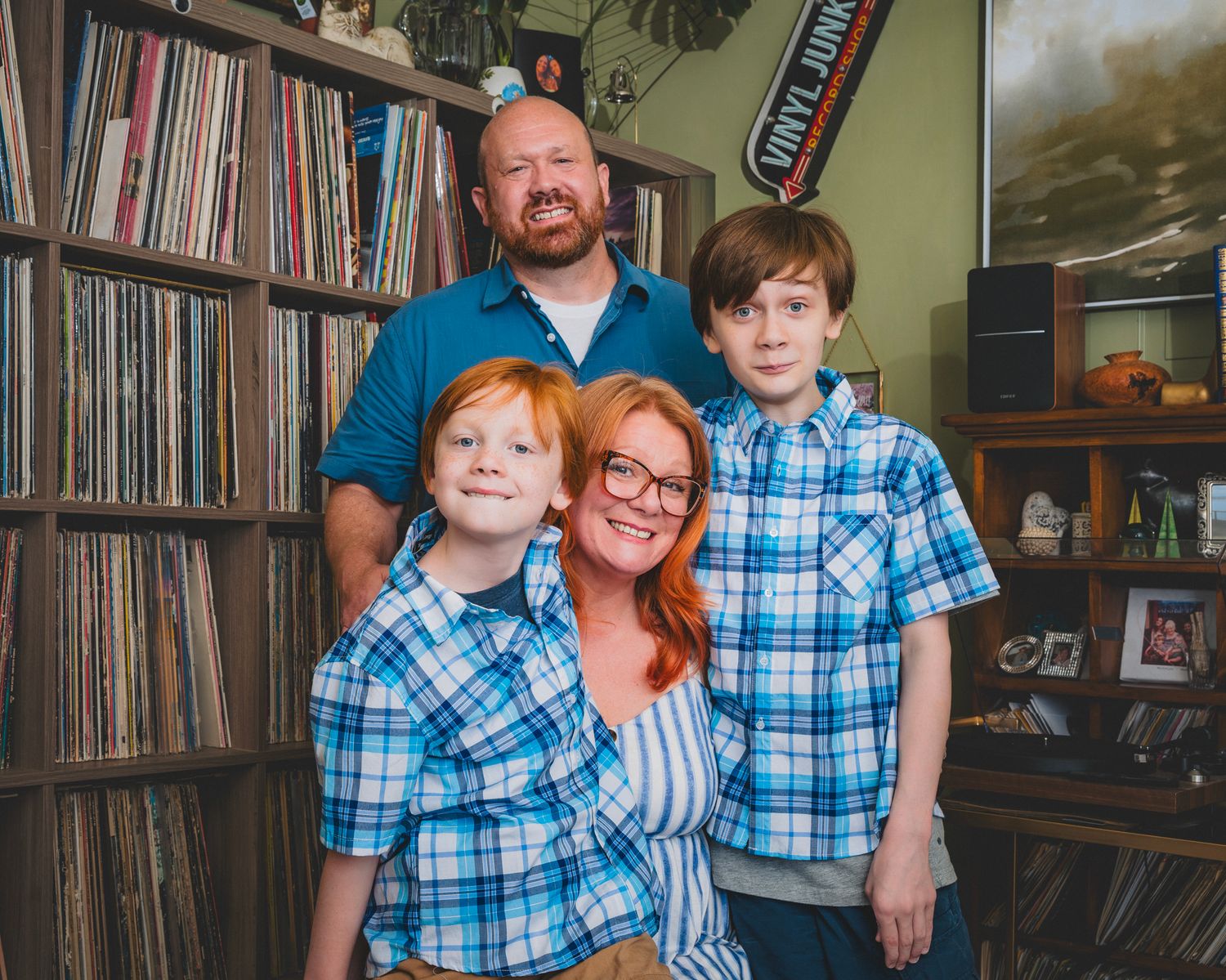 Family of four with red hair wearing matching blue plaid shirts posing in a vinyl record store.