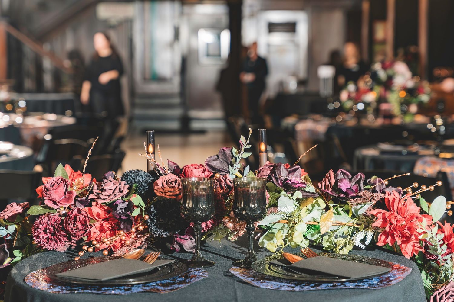 Elegant dark wedding tablescape with lush floral centerpiece of pink and purple blooms and dark glassware.