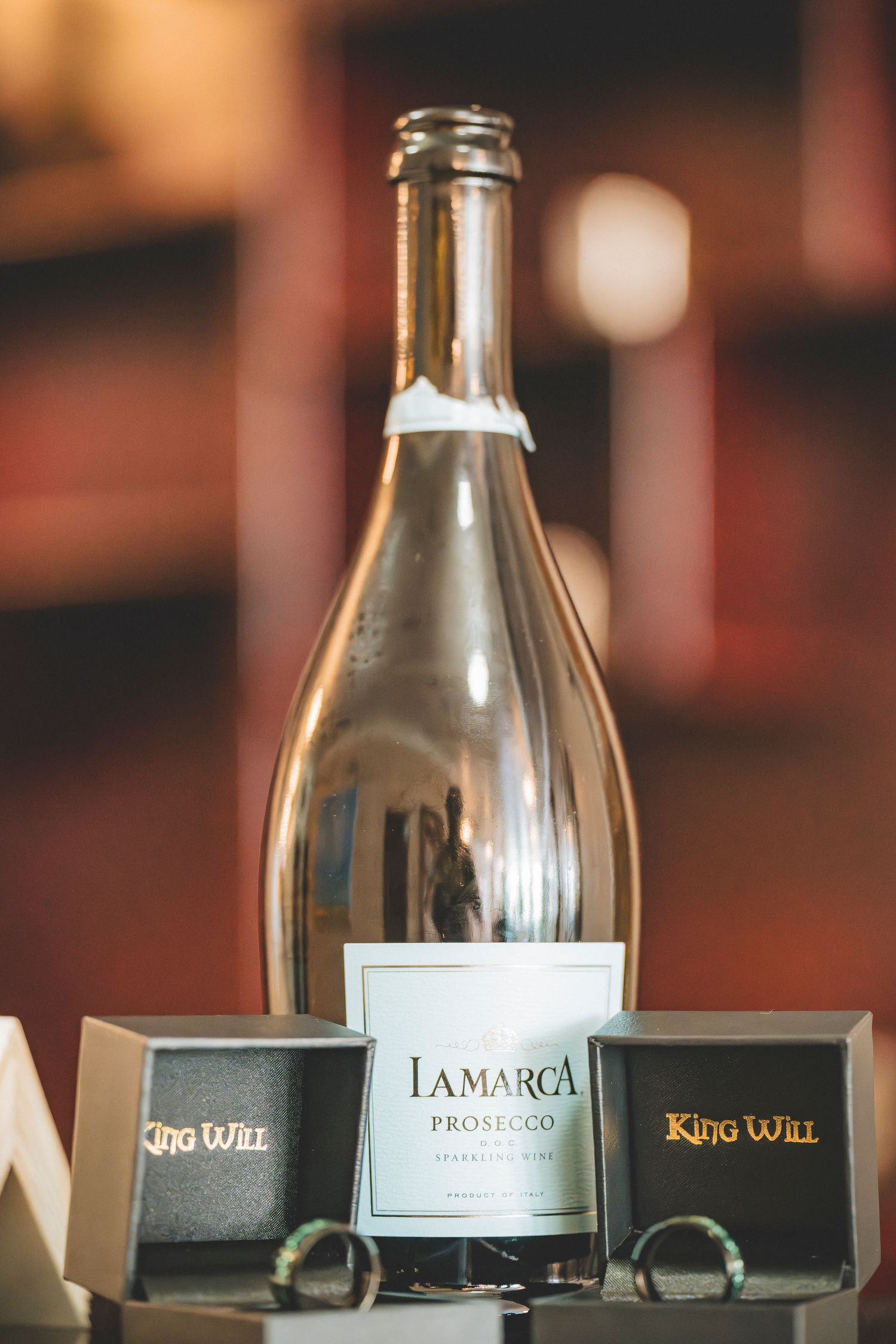 La Marca Prosecco sparkling wine bottle displayed with two King Will ring boxes at a wedding reception.