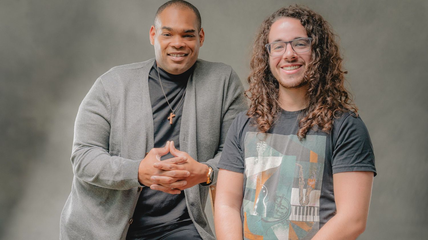 Two smiling men posing together for a casual portrait against a gray background.