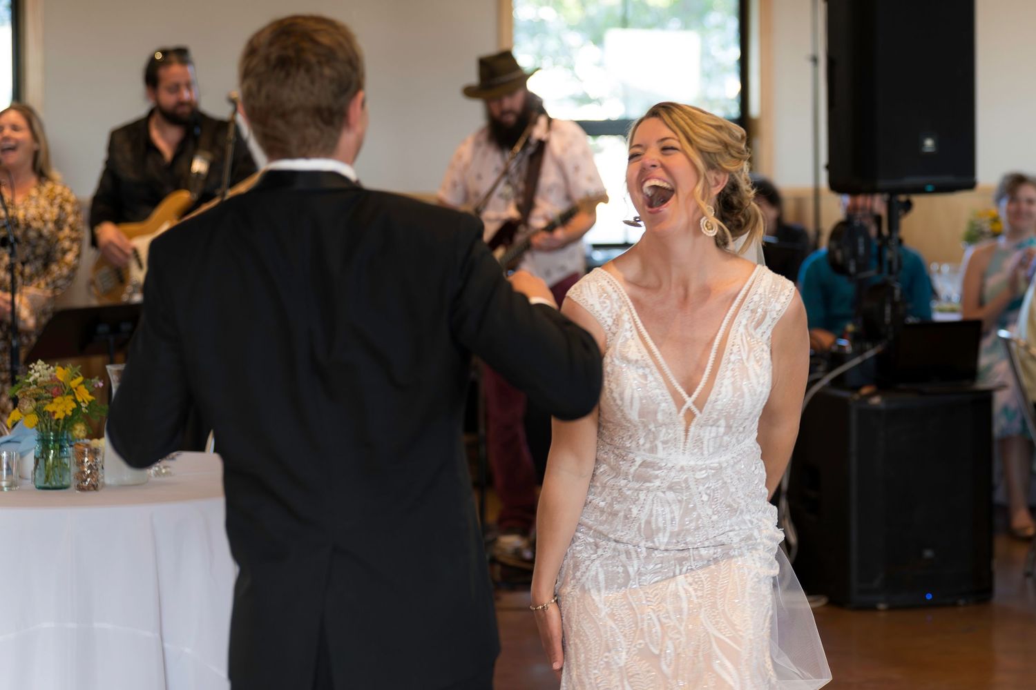 Bride laughing joyfully during first dance at wedding reception with live band performing in background.