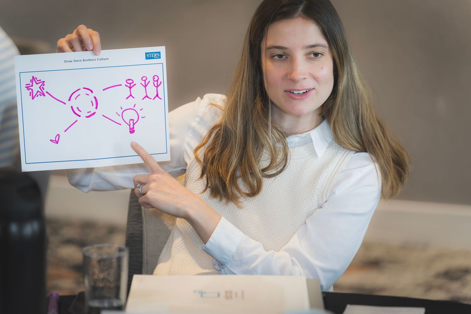 Young woman in white blouse presents hand-drawn diagram on tablet at business workshop.
