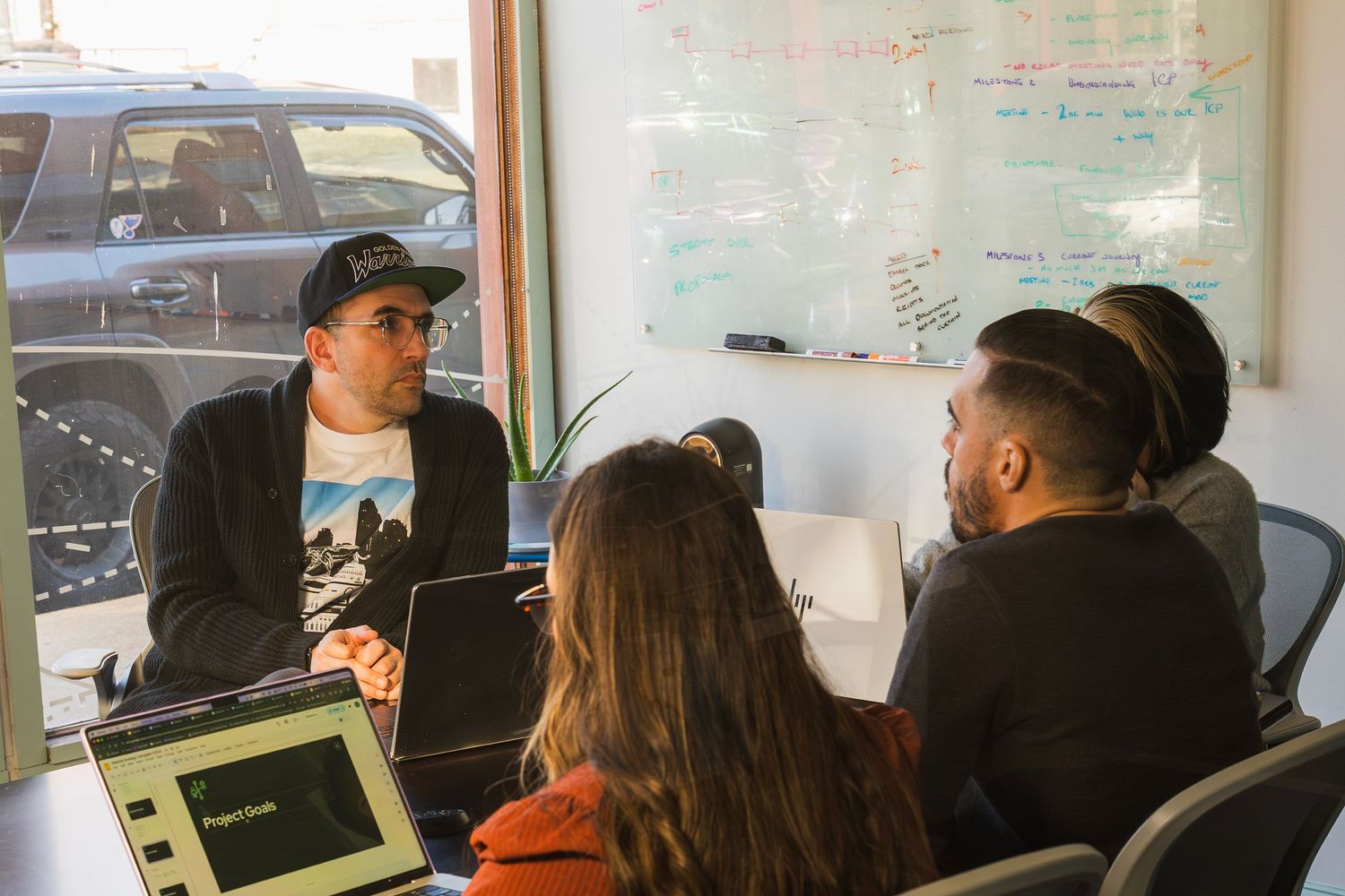 Three colleagues collaborating around a table with laptops in a bright modern office space.