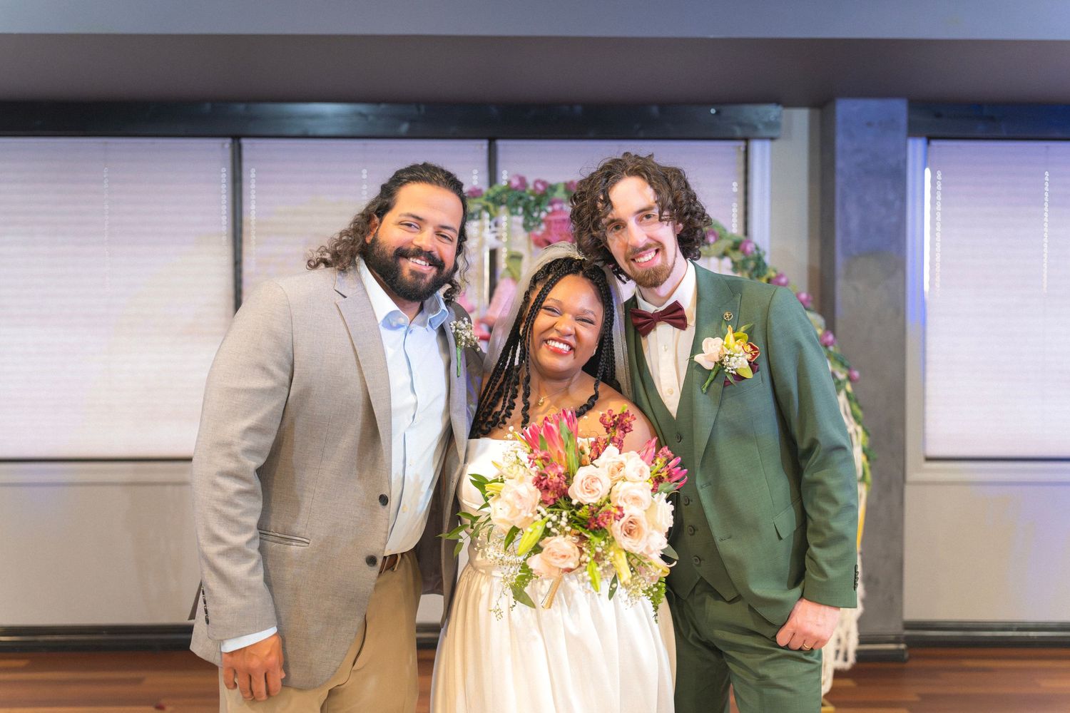 Bride and groom posing with officiant after wedding ceremony, bride holding vibrant bouquet, groom in green suit with bow tie.