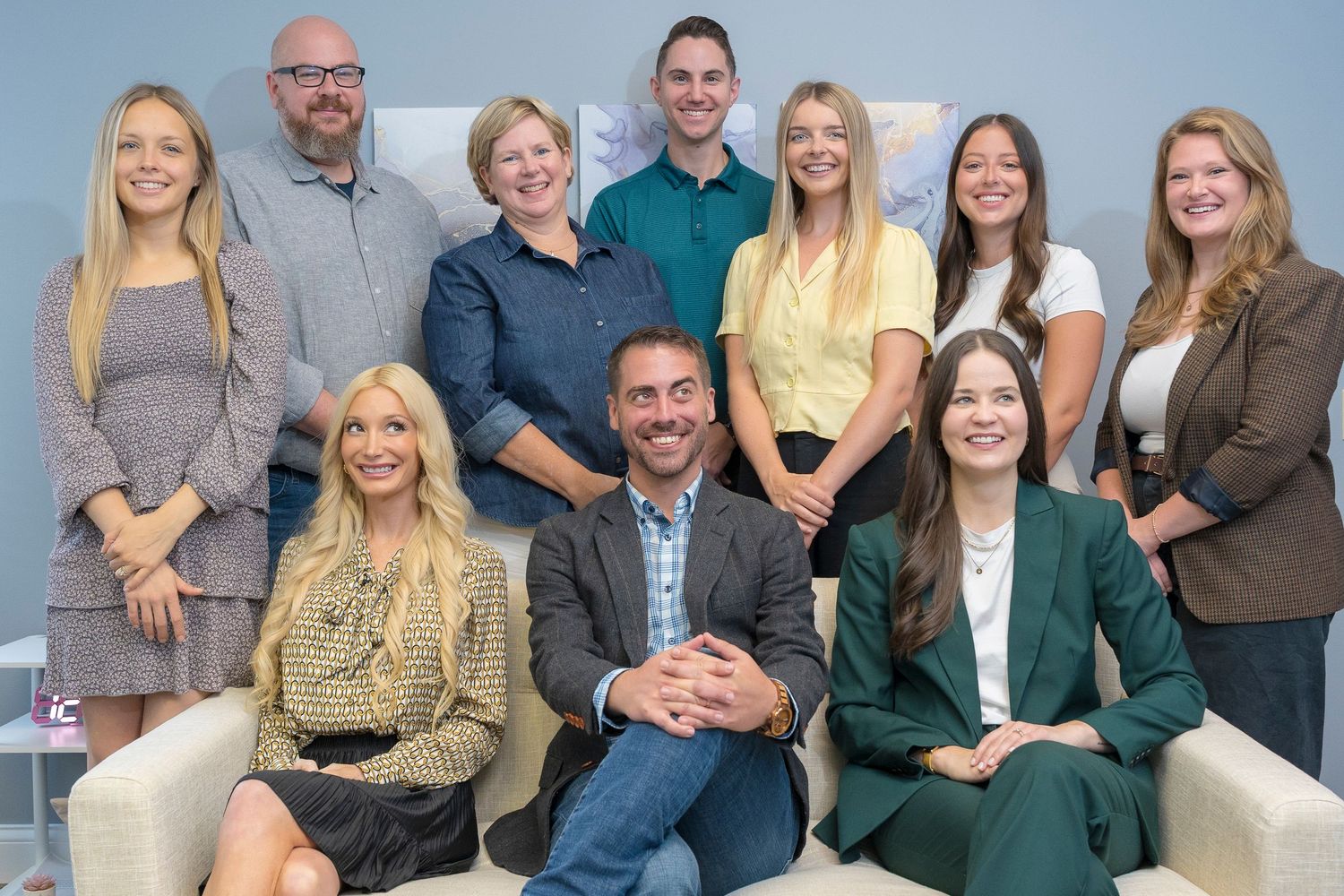 Professional team of ten smiling colleagues poses together in modern office setting.