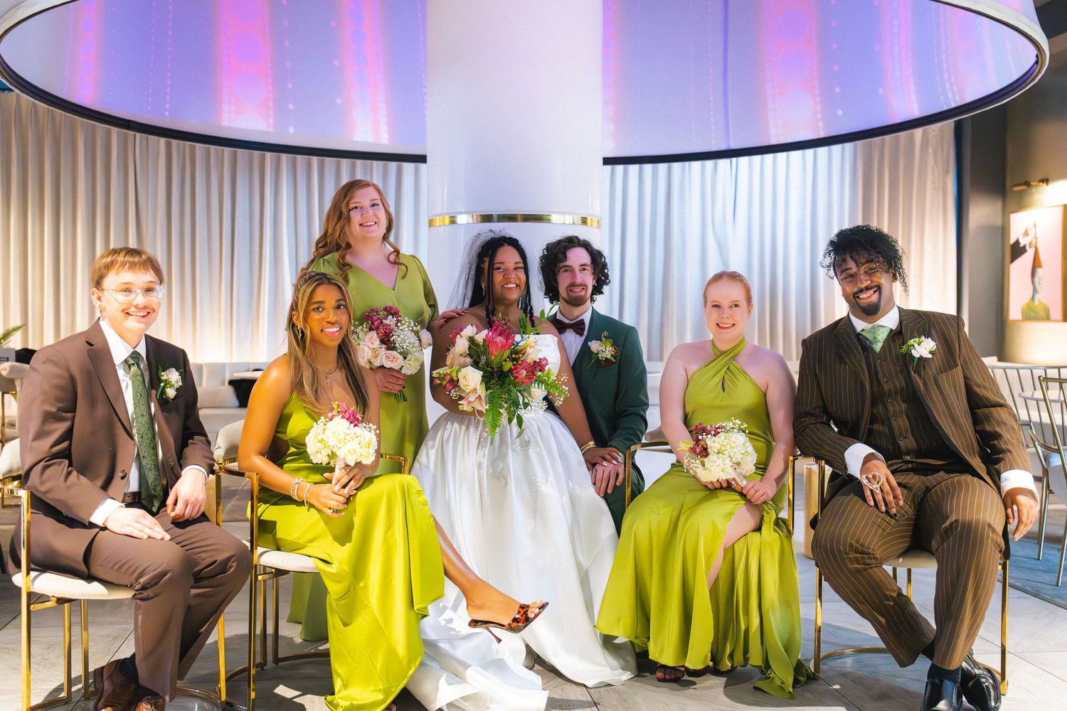 Wedding party posing together, bridesmaids in chartreuse dresses, groomsmen in brown suits, bride and groom in center.
