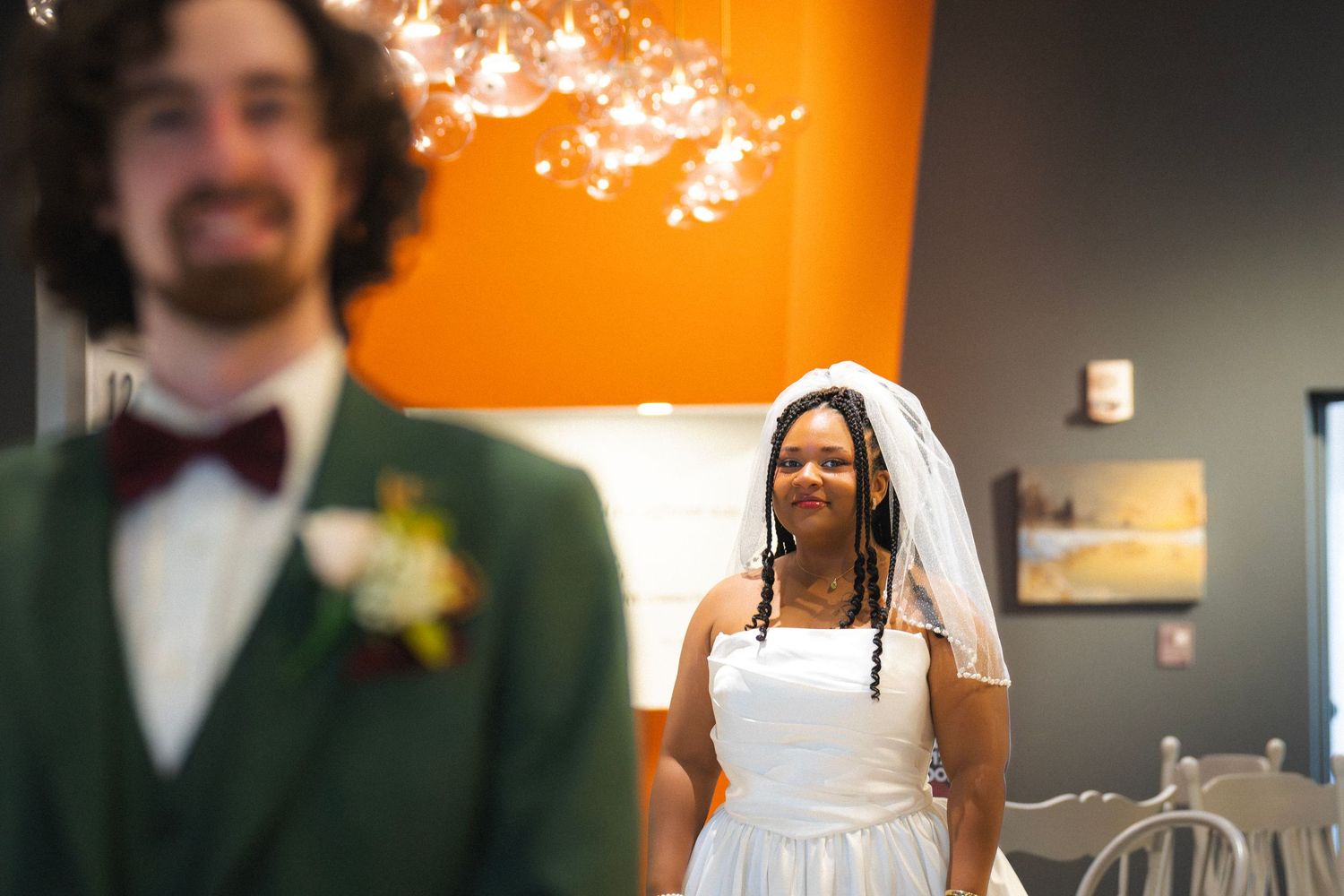 Bride smiles warmly at groom in green suit during emotional wedding first look moment.