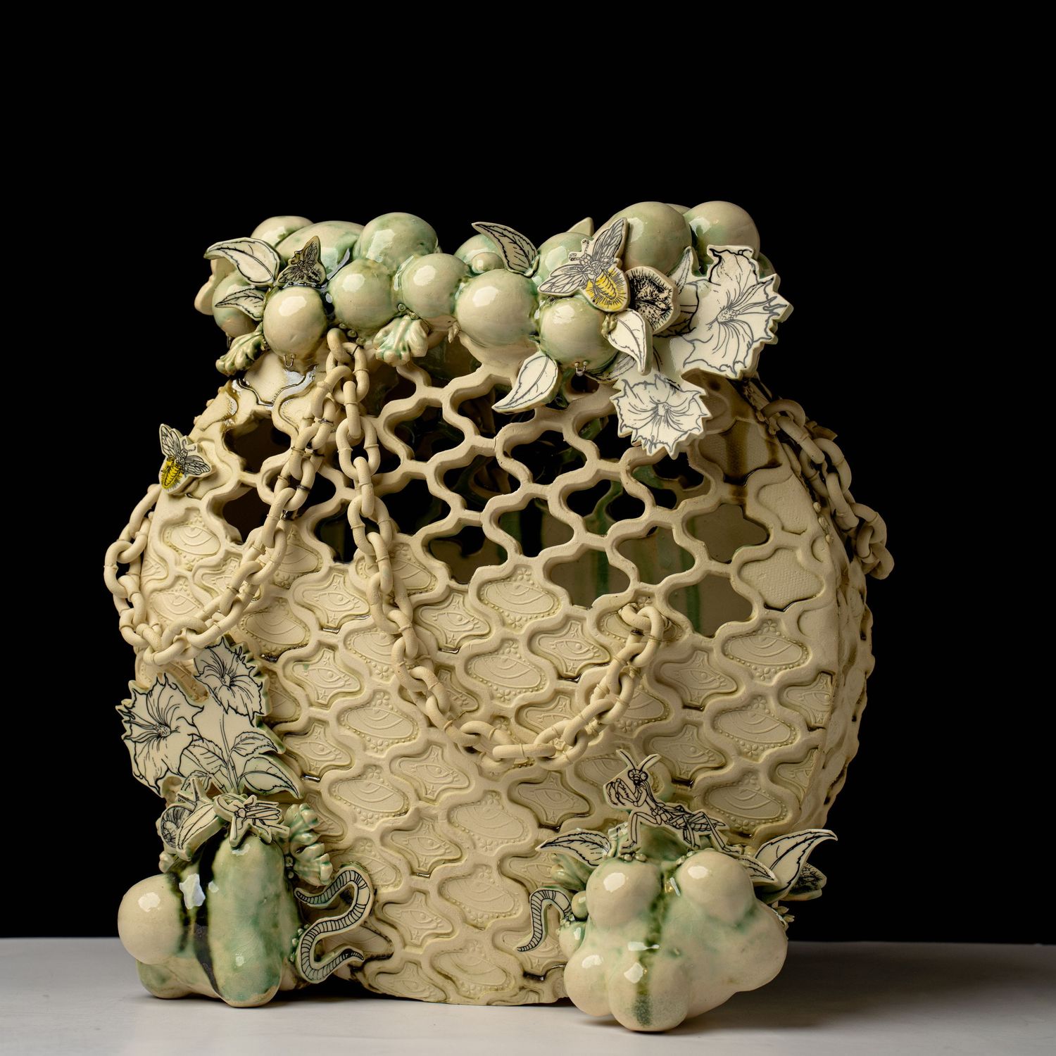 Decorative ceramic vase with lattice design, green fruit and leaf embellishments on neutral background.