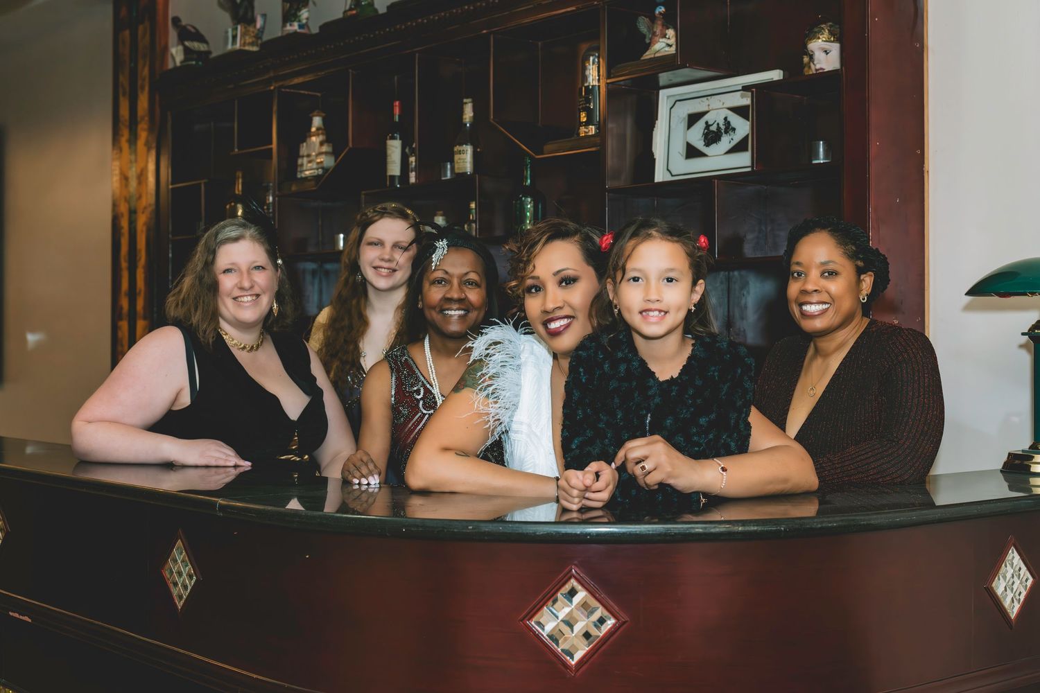 Five women smile together behind a bar counter at a wedding reception celebration.