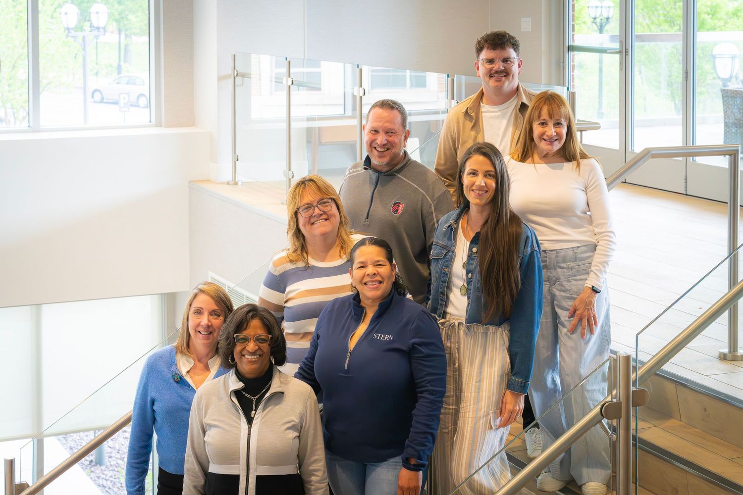 Group of eight diverse colleagues posing together on modern office staircase for team photo.