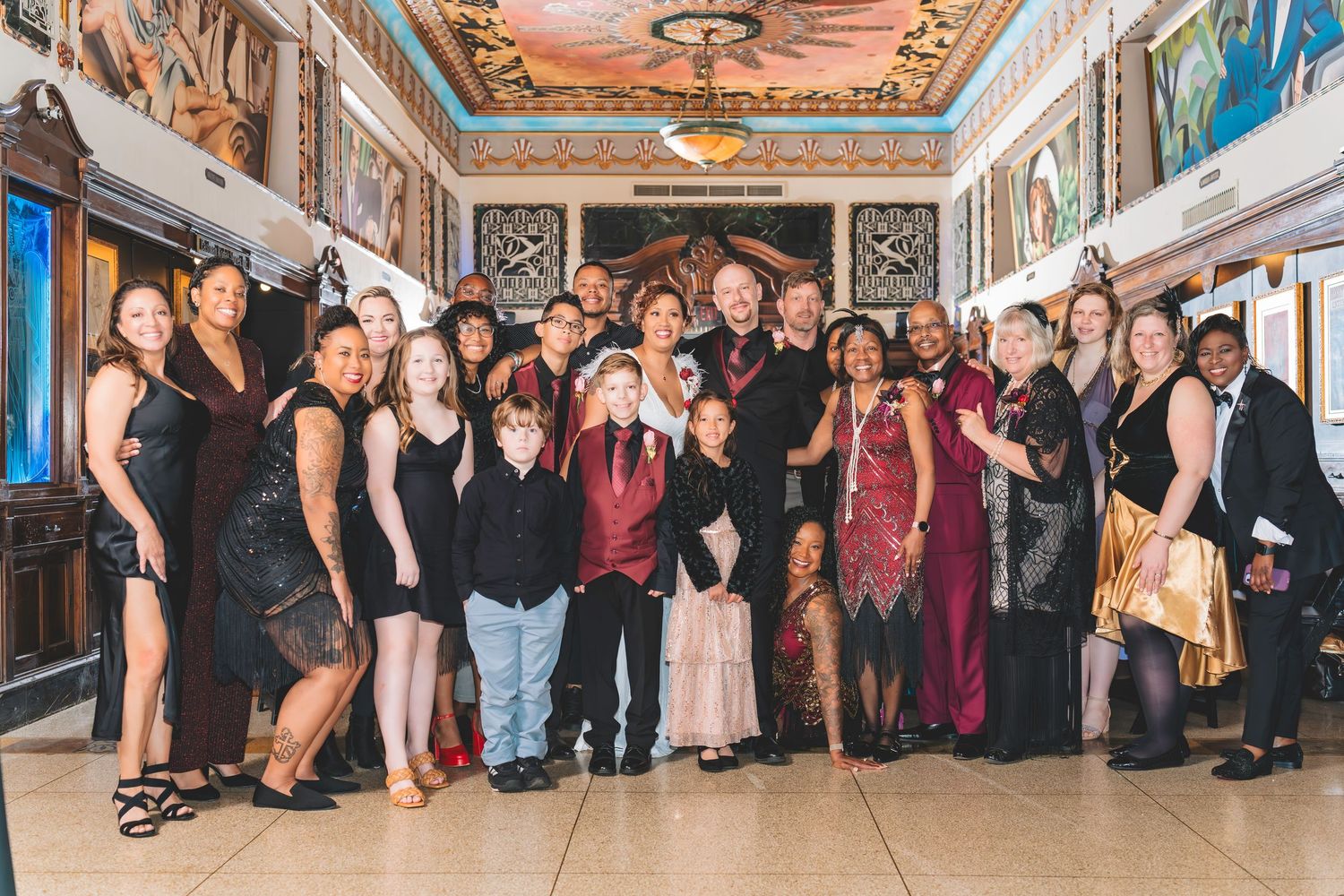 Wedding party group portrait in an elegant ornate venue with decorative ceiling and murals.