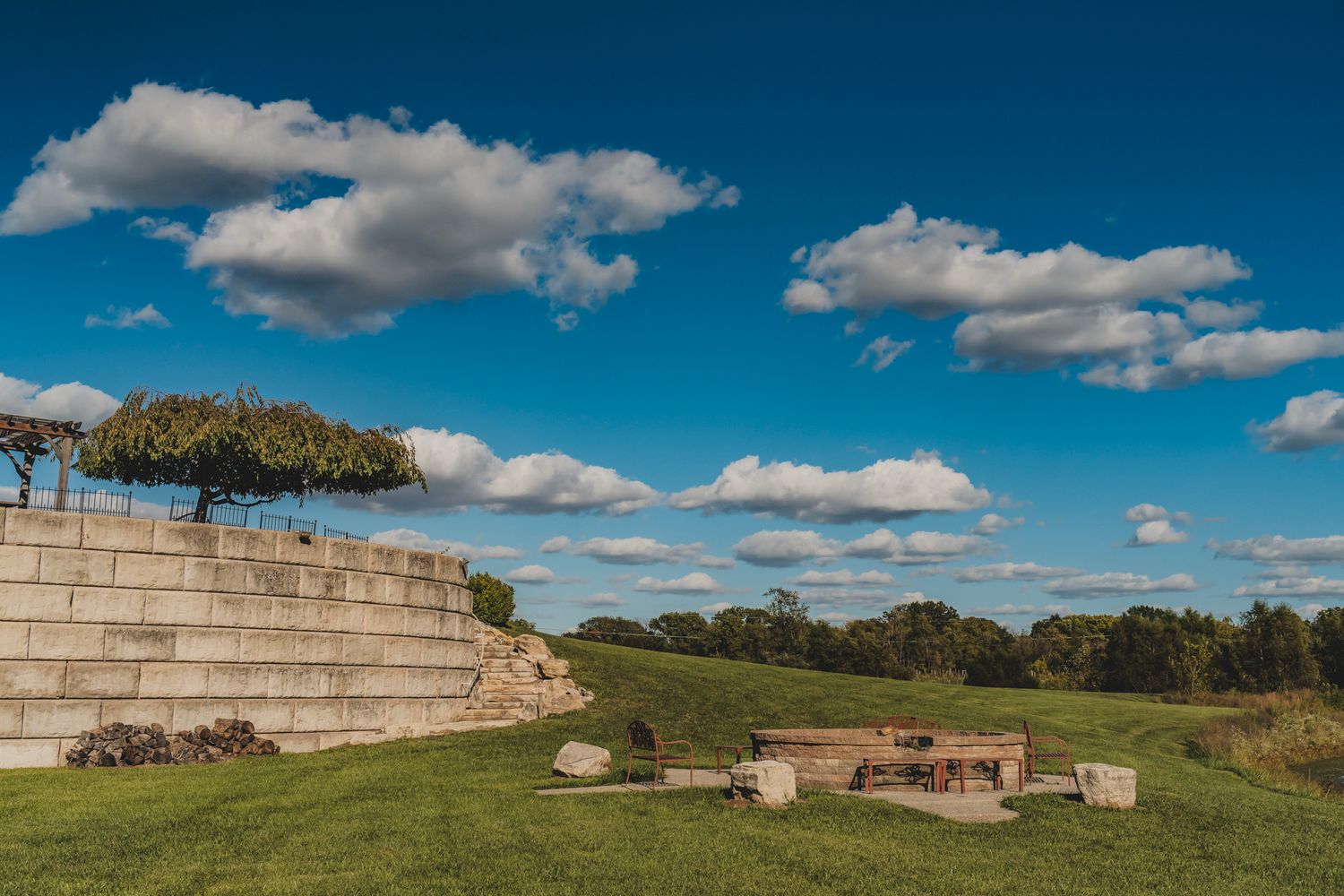 Scenic outdoor amphitheater with stone steps, green lawn, and blue cloudy sky.